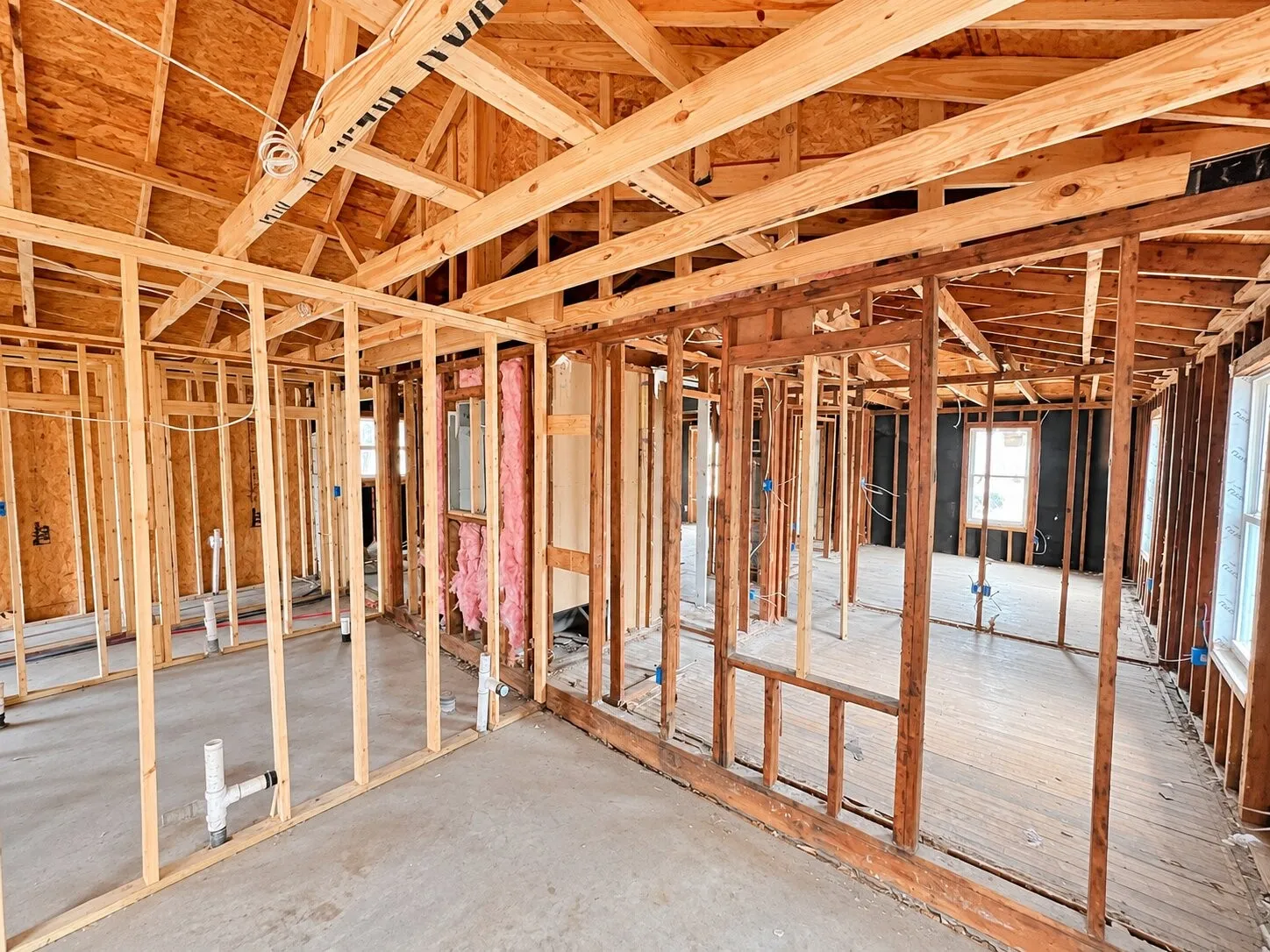 Exposed wood framing, vaulted ceiling structure, visible plumbing rough-ins, and unfinished window openings