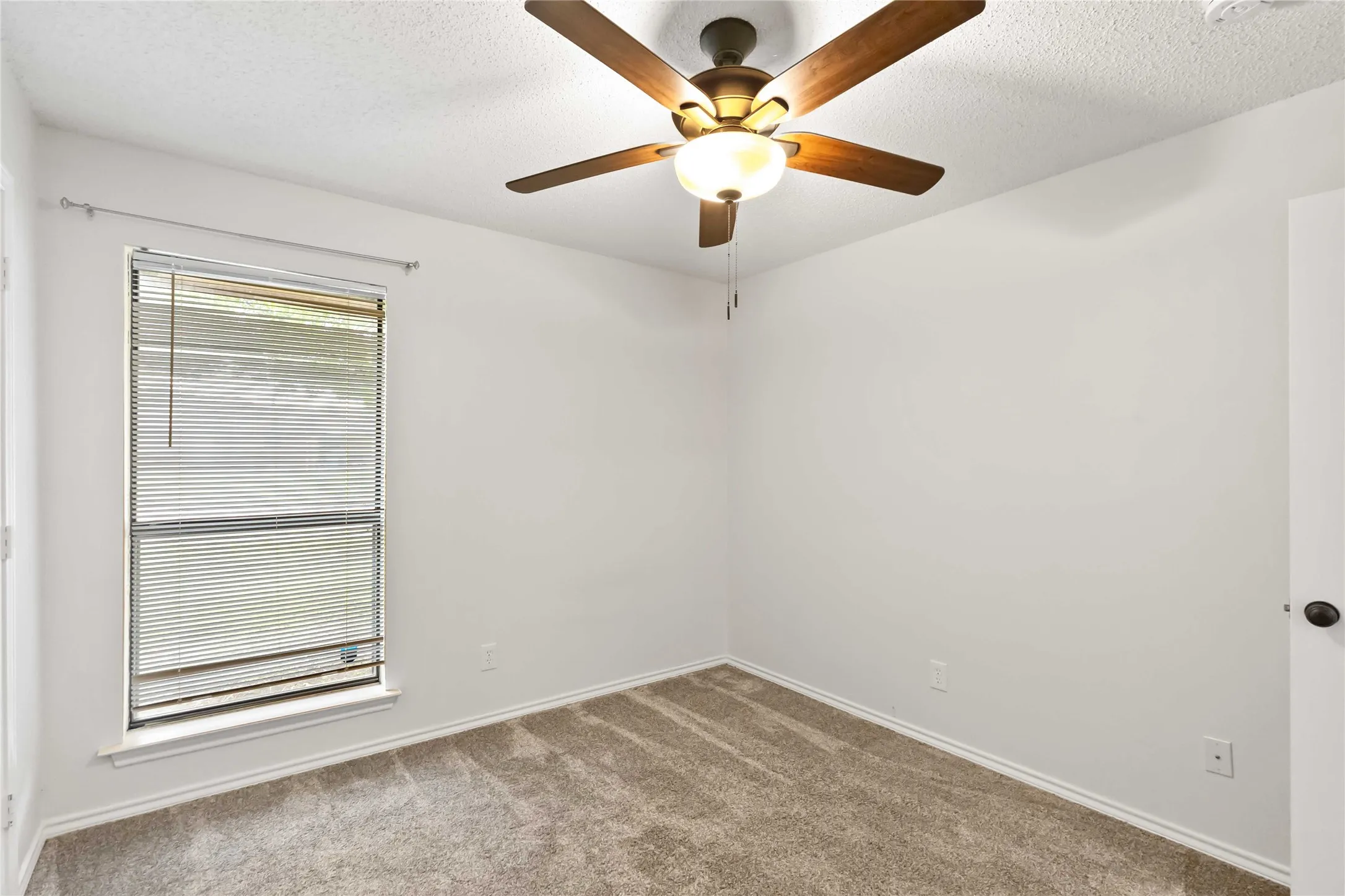 Bedroom featuring neutral carpeting, a double-hung window with blinds, and a ceiling fan with integrated lighting
