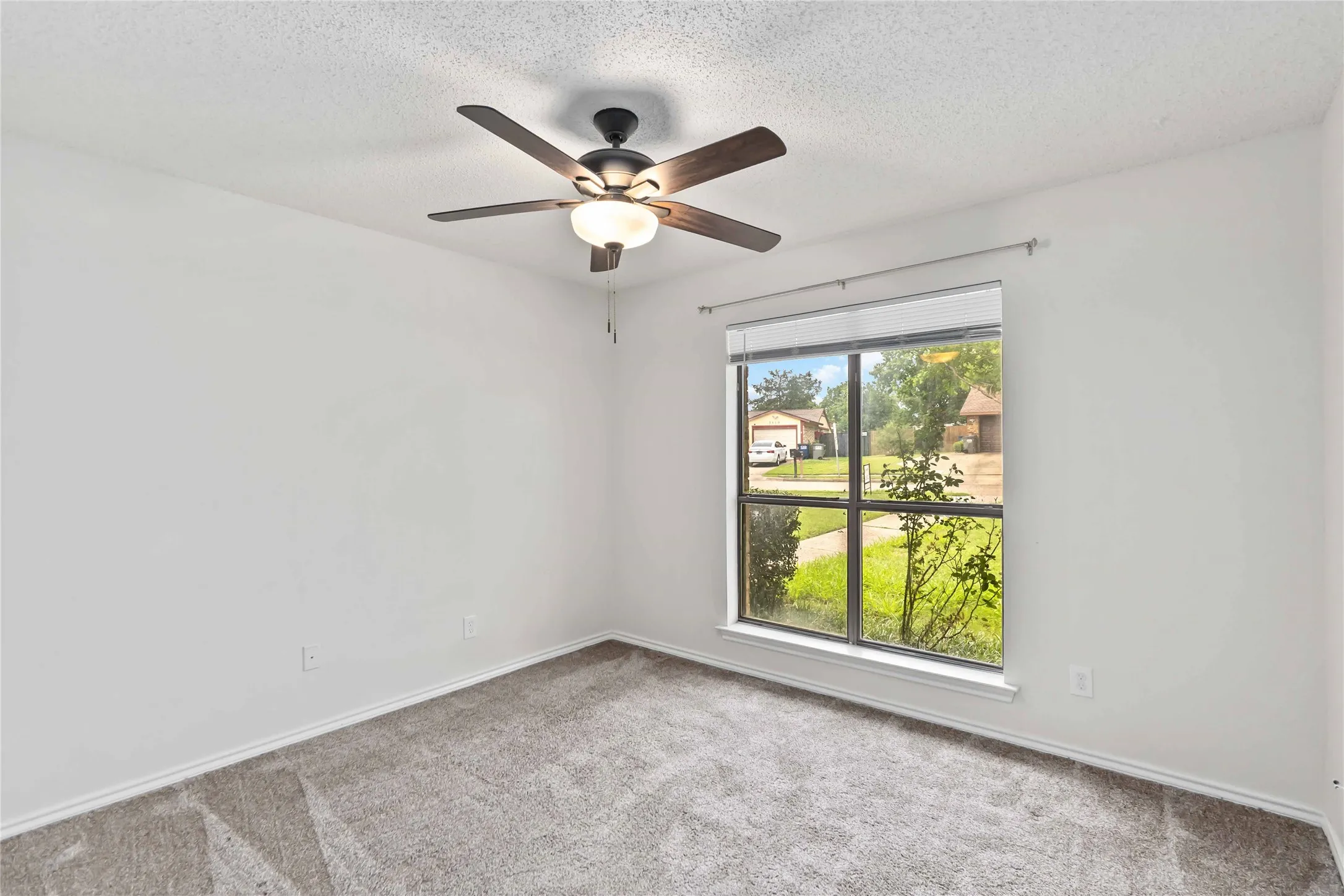 Interior room featuring neutral wall paint, gray patterned carpet flooring, a ceiling fan with integrated lighting, and a large window with white trim