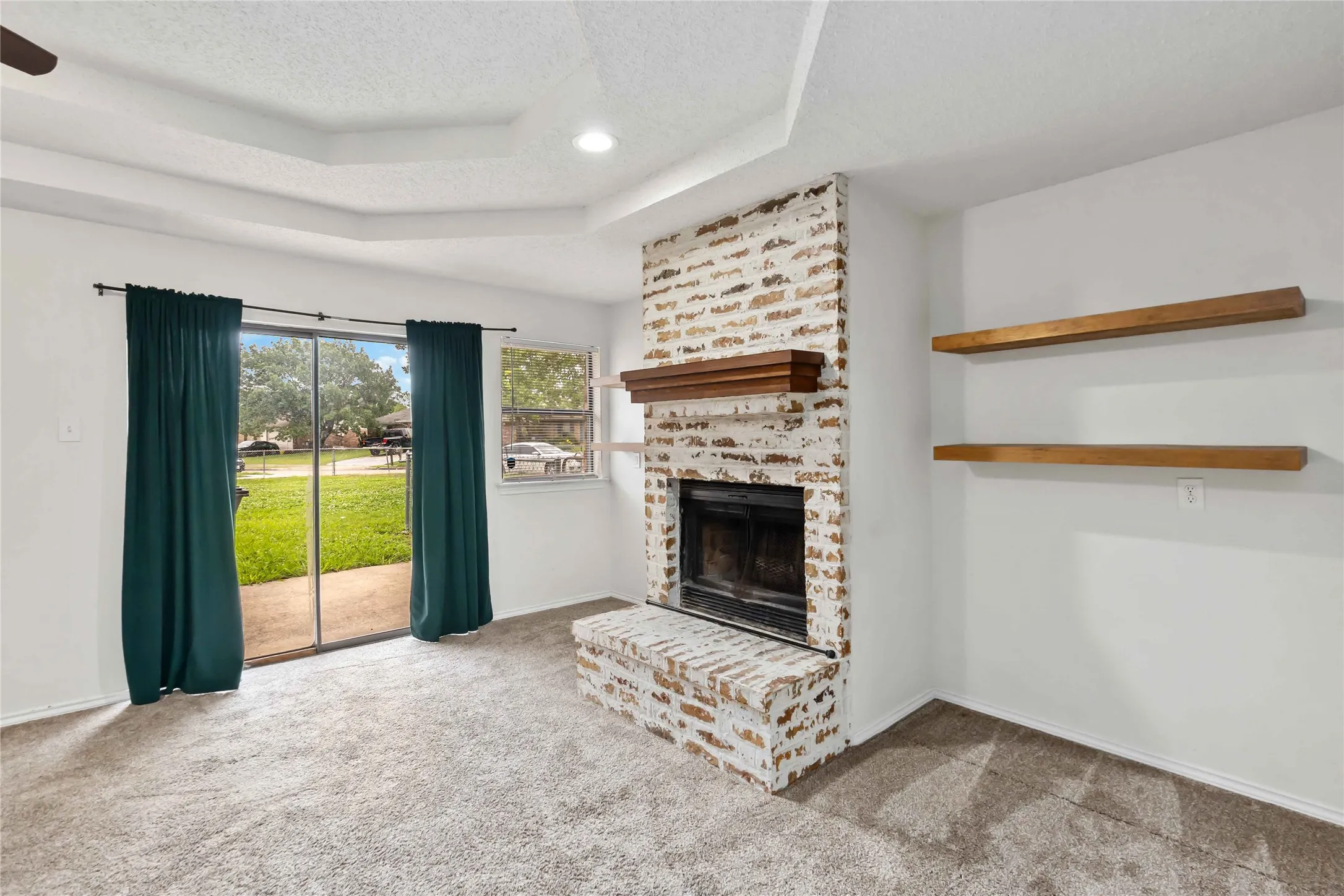 Living space featuring a whitewashed brick fireplace with a wood mantel, tray ceiling, and recessed lighting