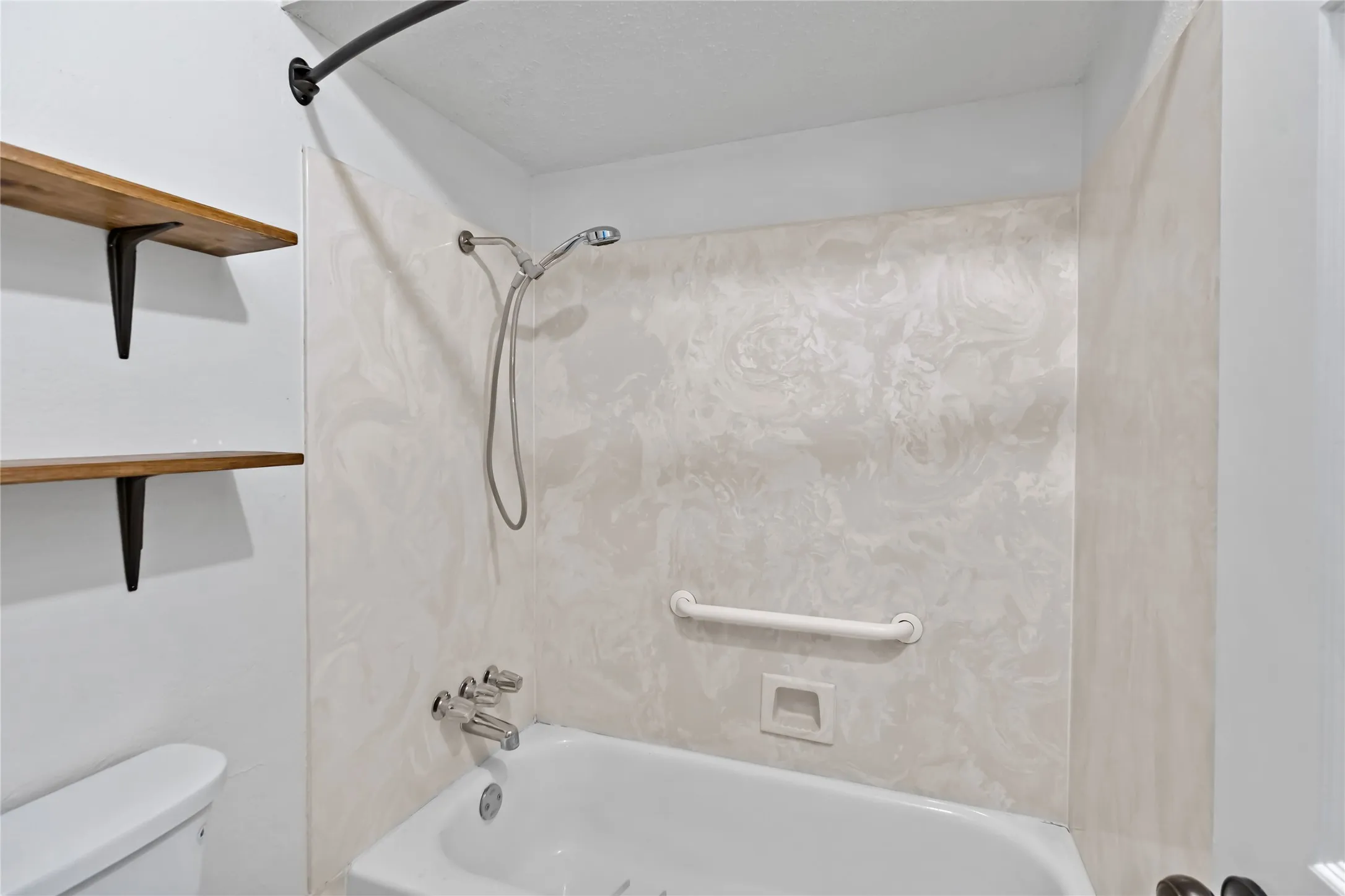 Tub/shower combination featuring a white tub, chrome fixtures, and a light-toned patterned surround