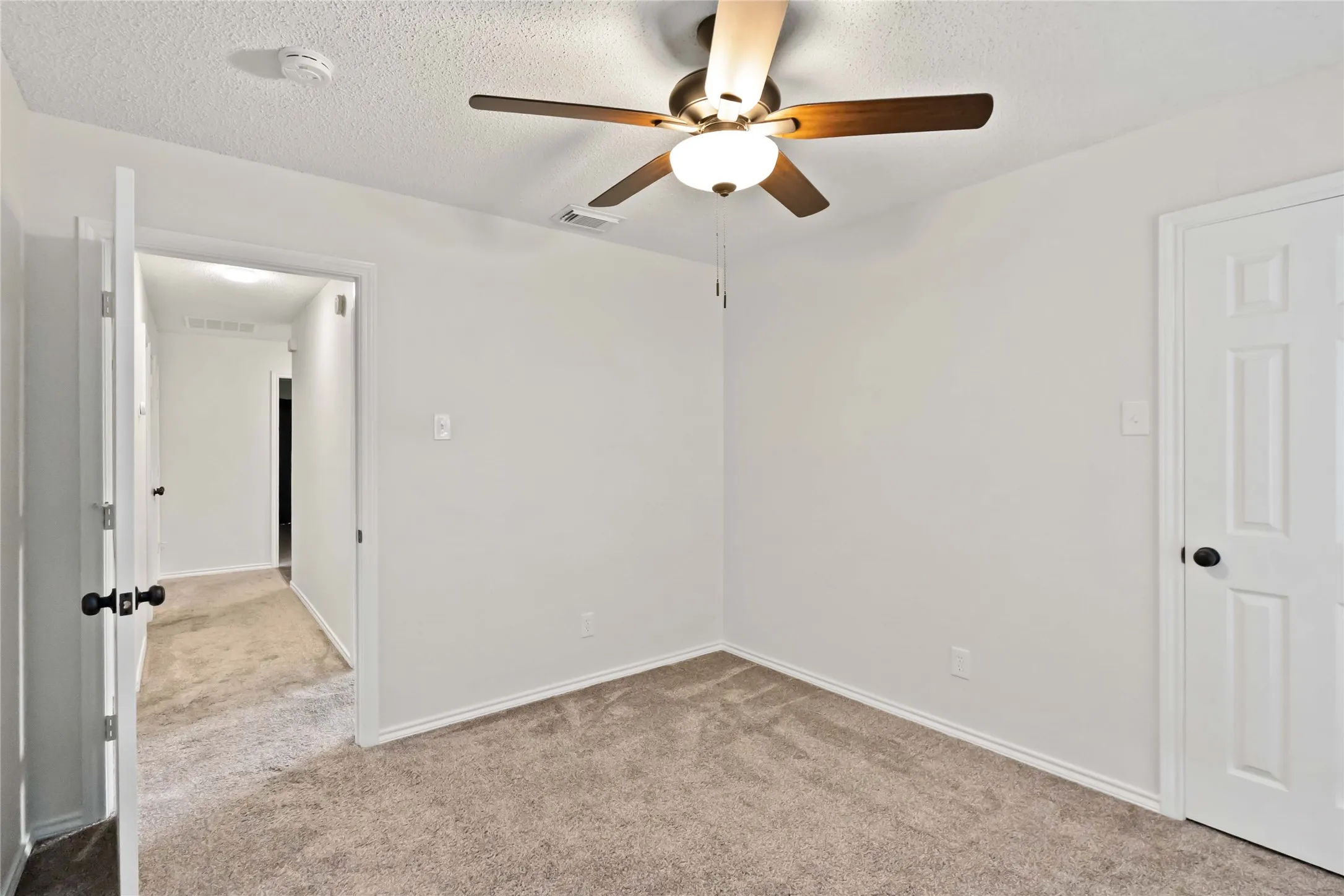 Carpeted room with a ceiling fan light fixture, white walls, and white trim
