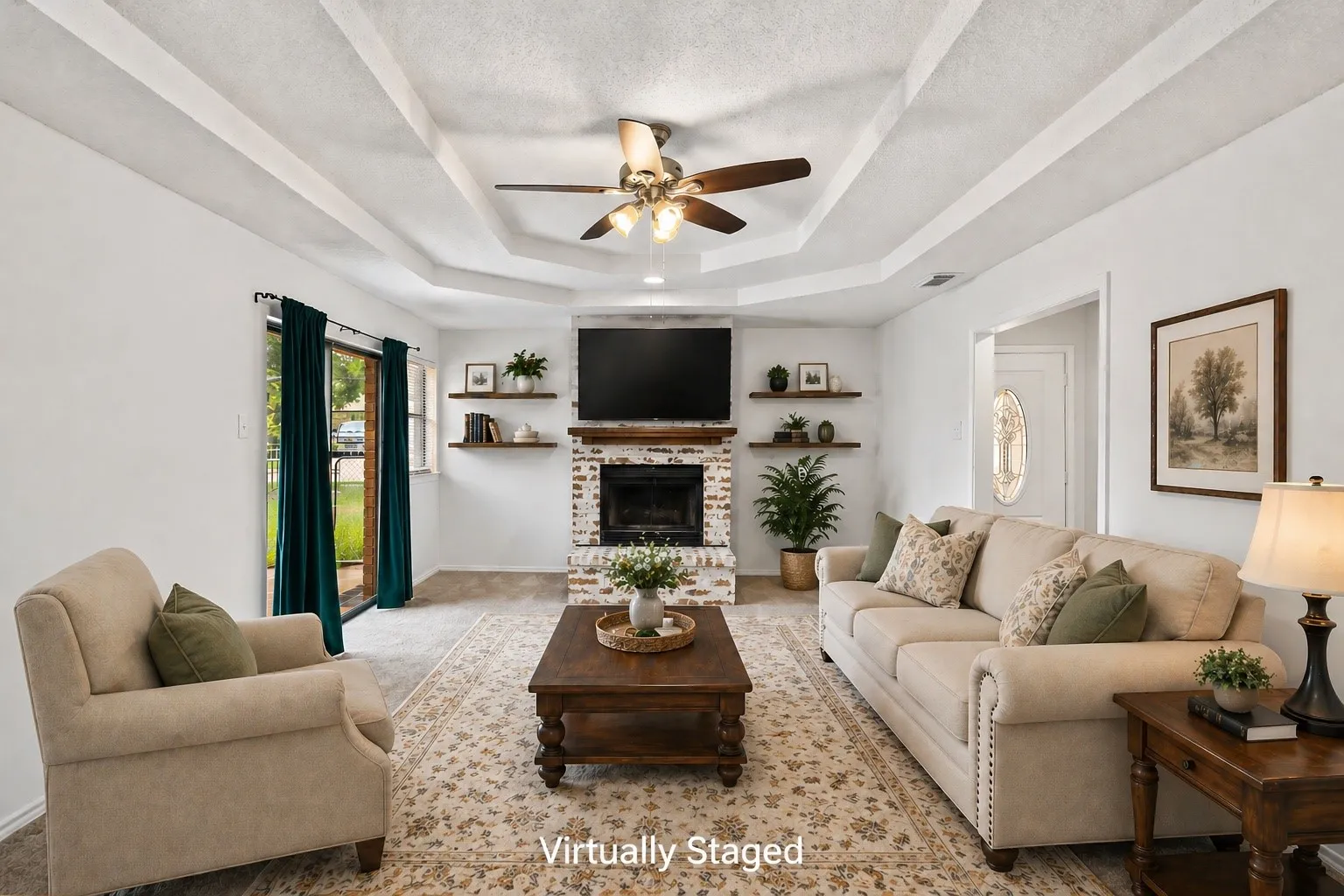 Living area featuring a white-painted brick fireplace with a wood mantel, tray ceiling, ceiling fan, and sliding glass door