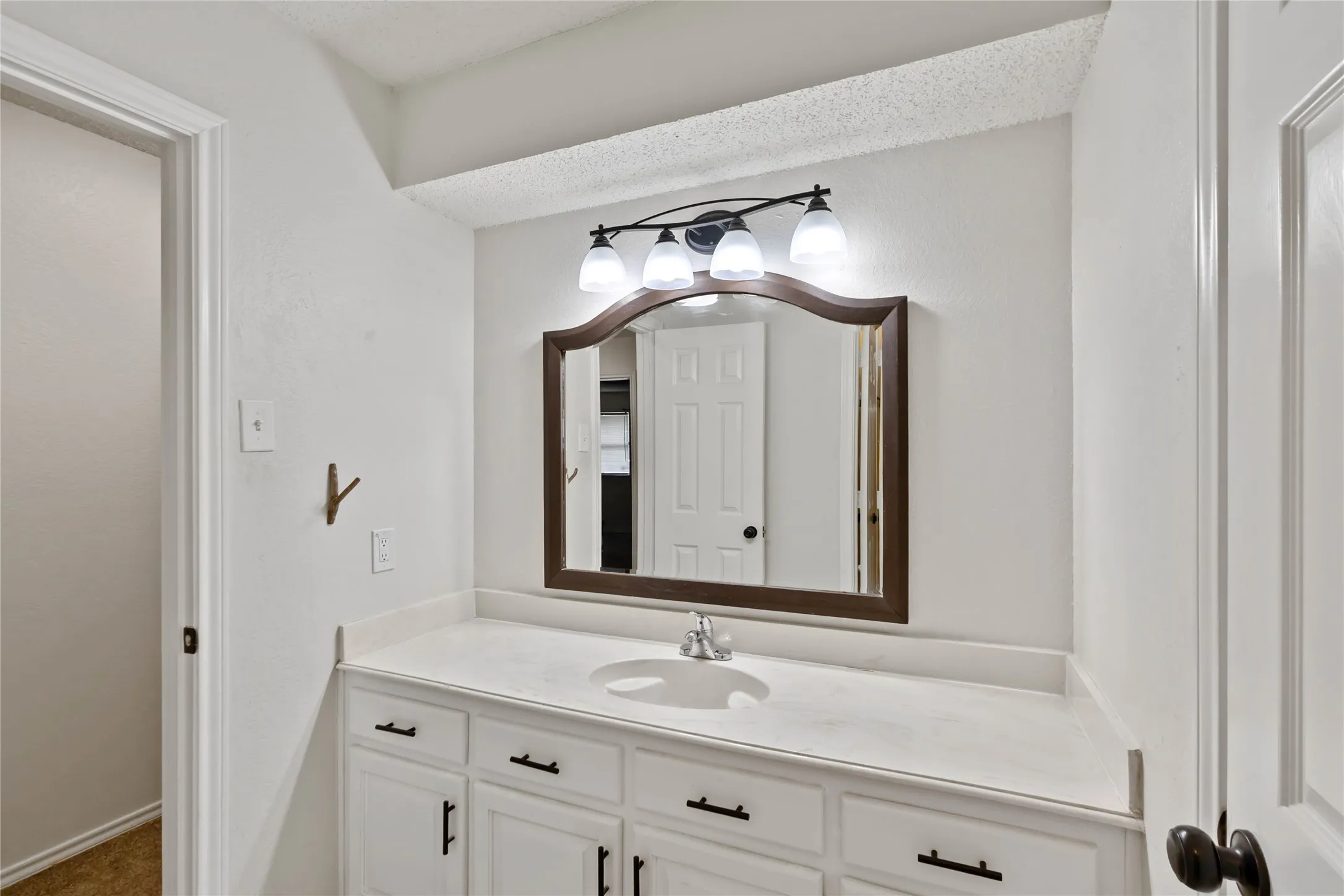 Bright bathroom vanity featuring a white countertop, undermount sink, and dark wood-framed mirror