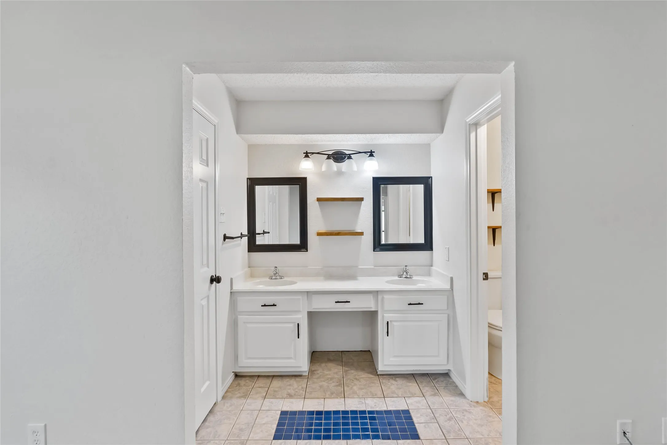 Bathroom featuring a dual vanity with white cabinetry, integrated sinks, black framed mirrors, and a black three-light fixture
