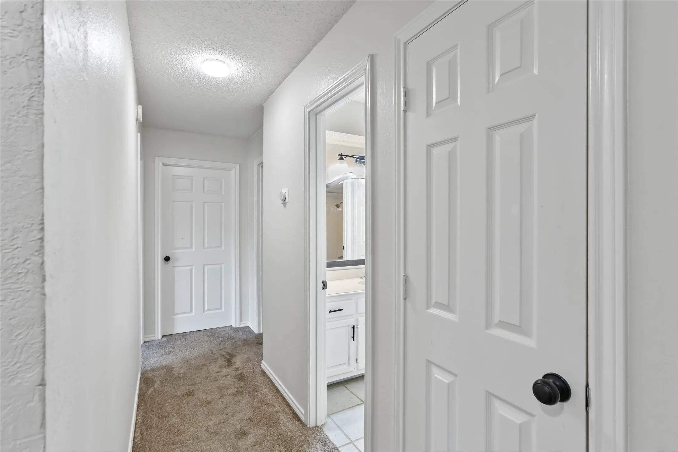 Hallway with light-colored carpet flooring and white painted walls
