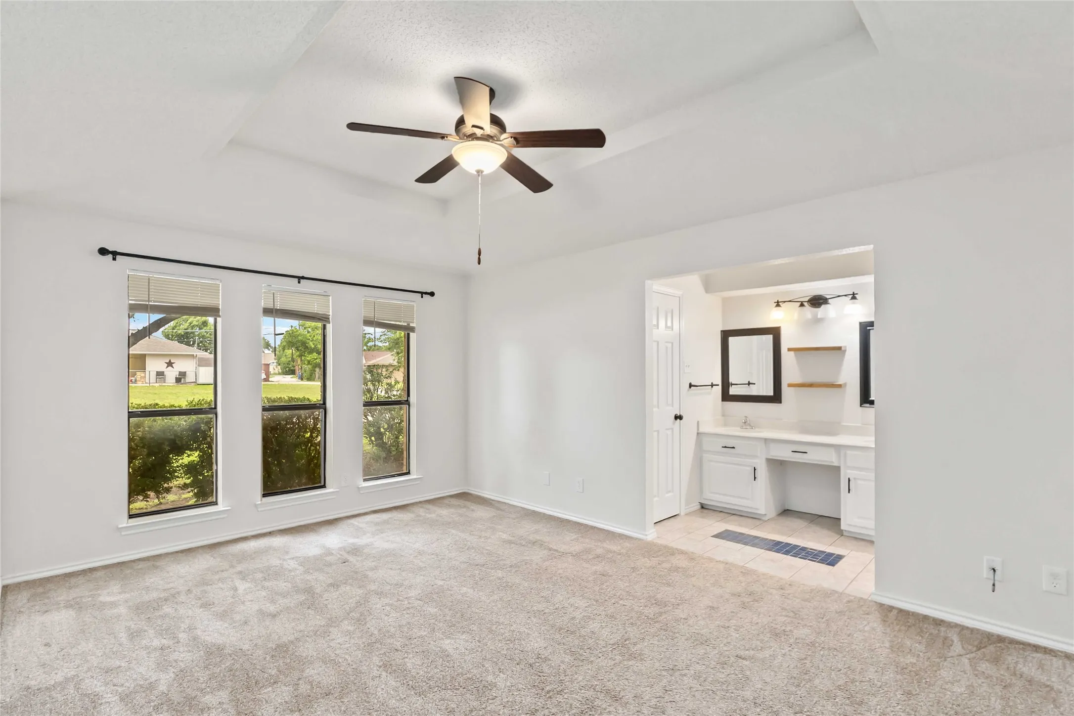 Spacious room featuring a tray ceiling, ceiling fan, and triple windows with outdoor scenery