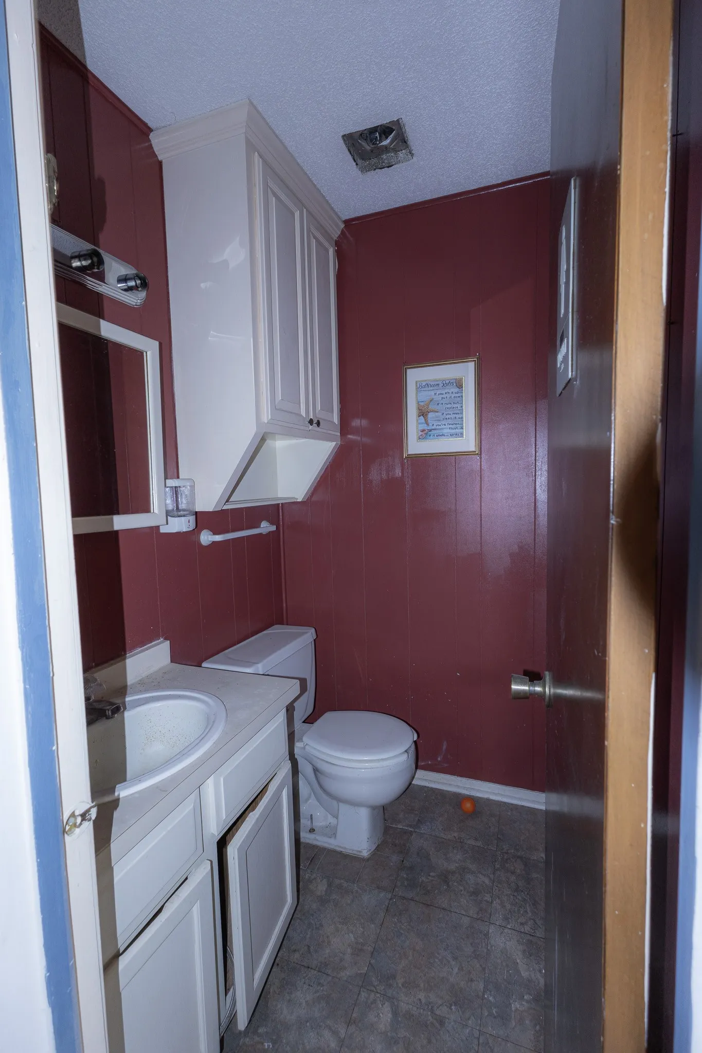 White vanity with integrated sink, paneling, and an overhead storage cabinet
