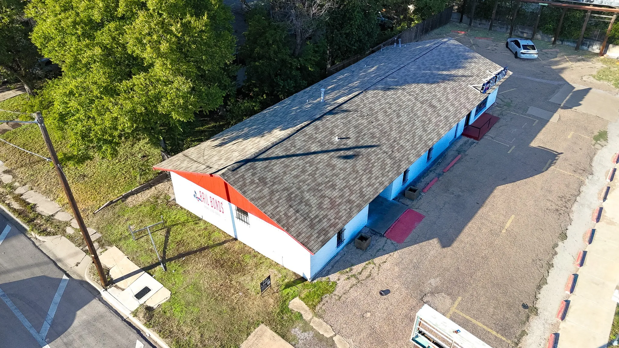 Long-span building with a shingle roof, a red fascia, and multiple windows