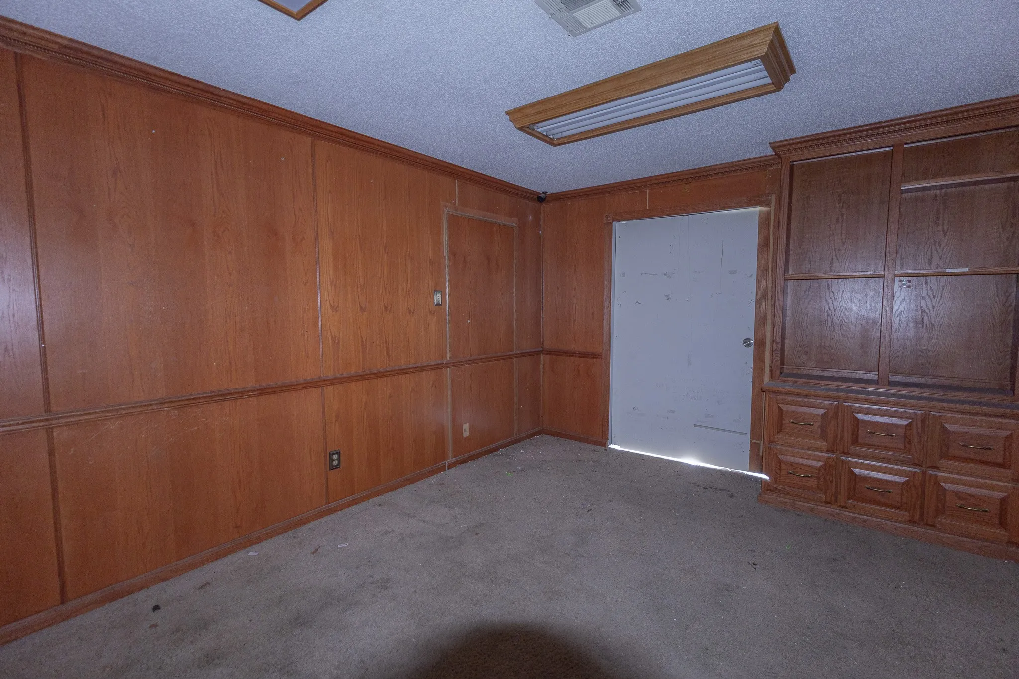 Wood paneling throughout, built-in wooden cabinetry with multiple drawers and glass-front upper cabinets, and a drop ceiling with a fluorescent light fixture