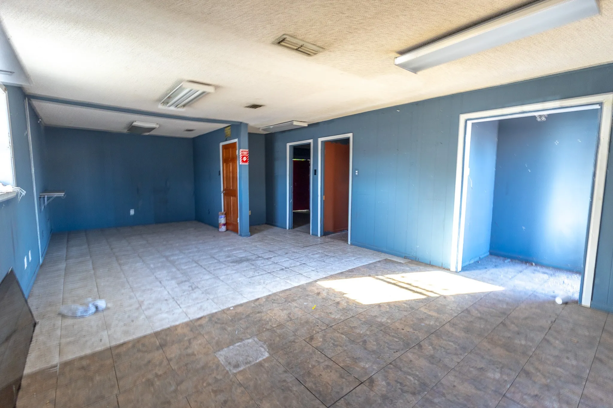 Spacious room featuring multiple doorways, recessed lighting, and a combination of tiled and wood-finish flooring