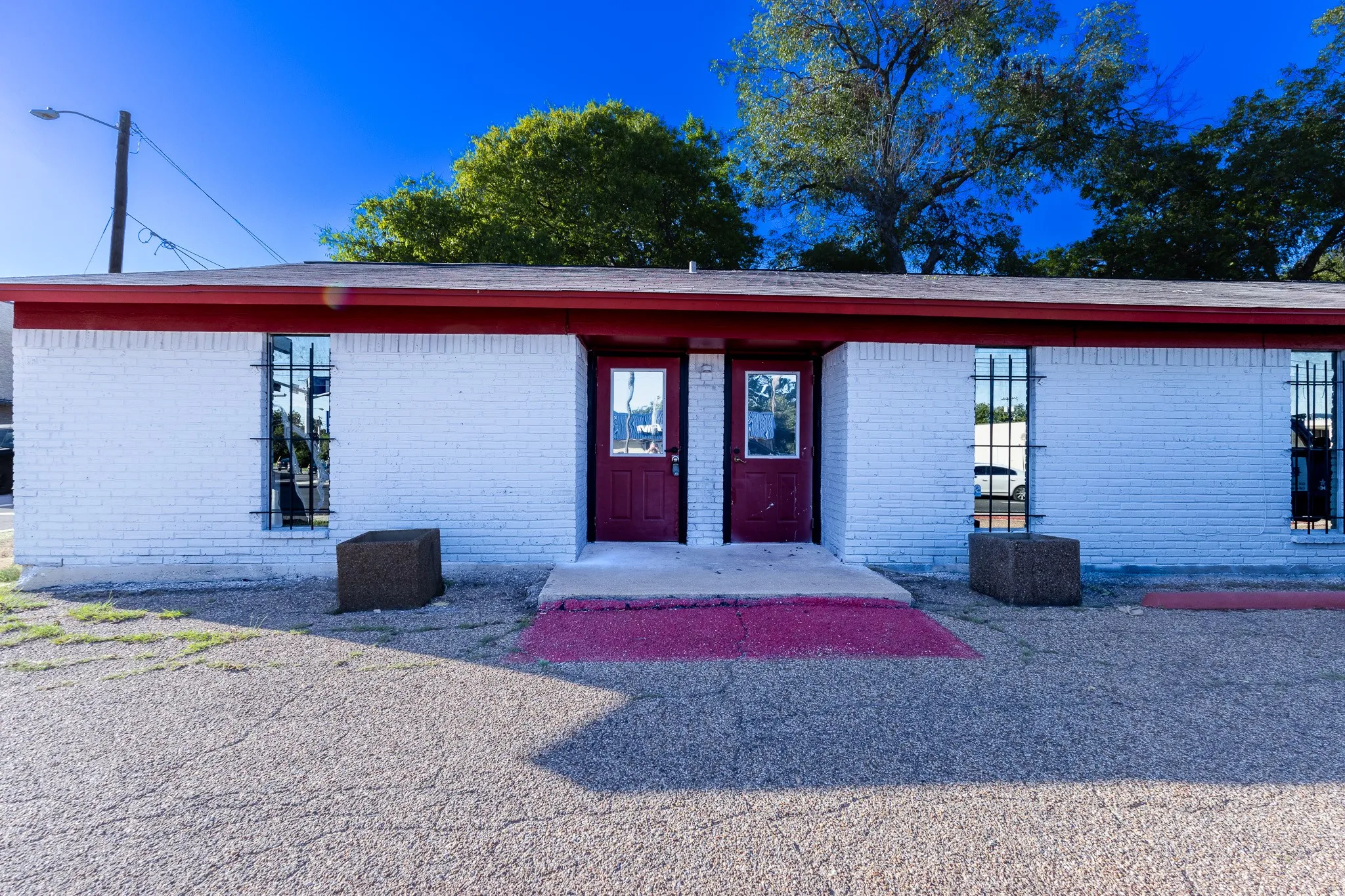 White brick exterior with a red trim roofline, two entry doors, and windows with security bars