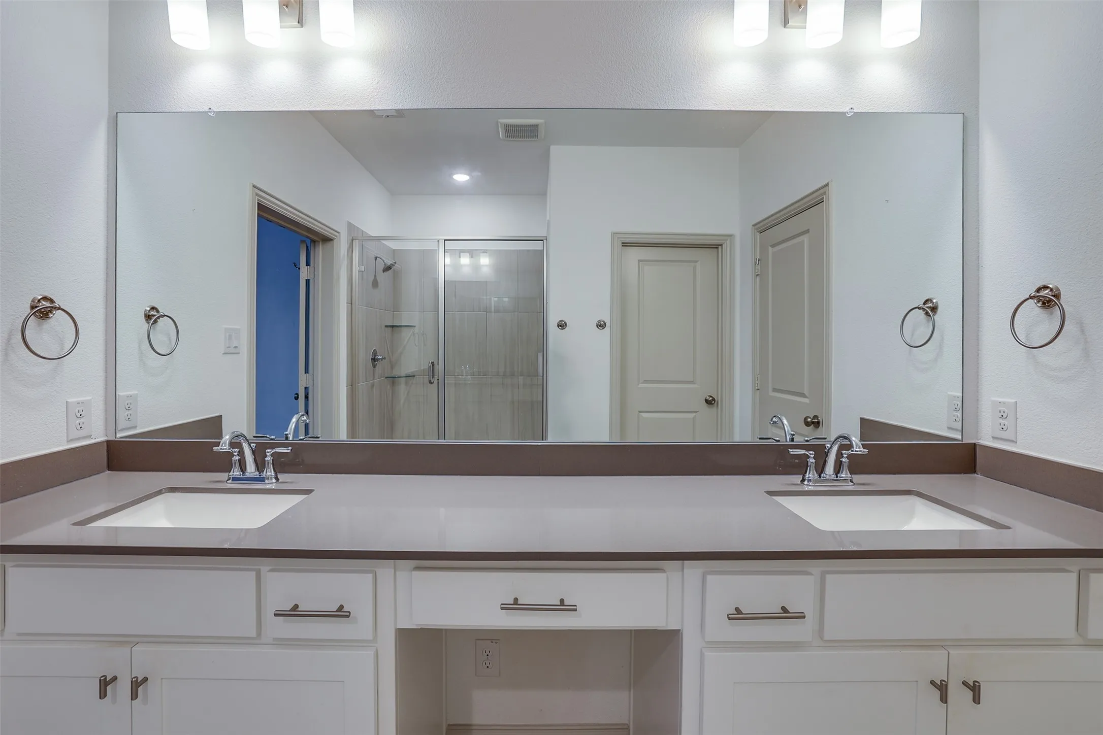 Dual undermount sinks with chrome fixtures, a full-width vanity mirror, and white cabinetry with brushed nickel hardware