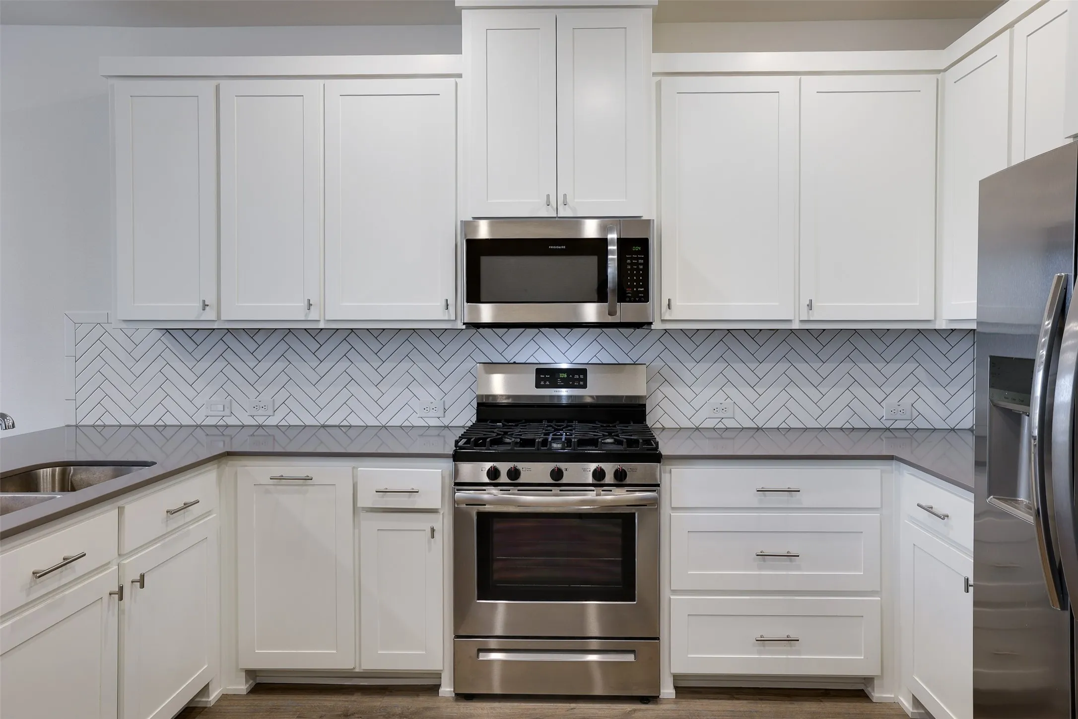 White shaker-style cabinetry, stainless steel appliances, herringbone tile backsplash, double basin sink, and ample counter space