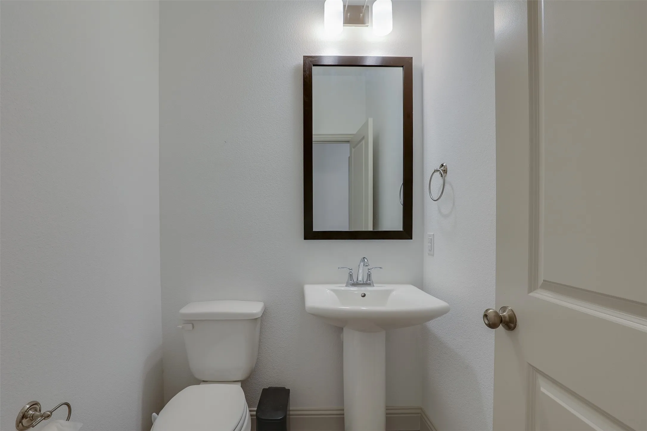 Pedestal sink with chrome faucet, framed mirror, and wall-mounted light fixture