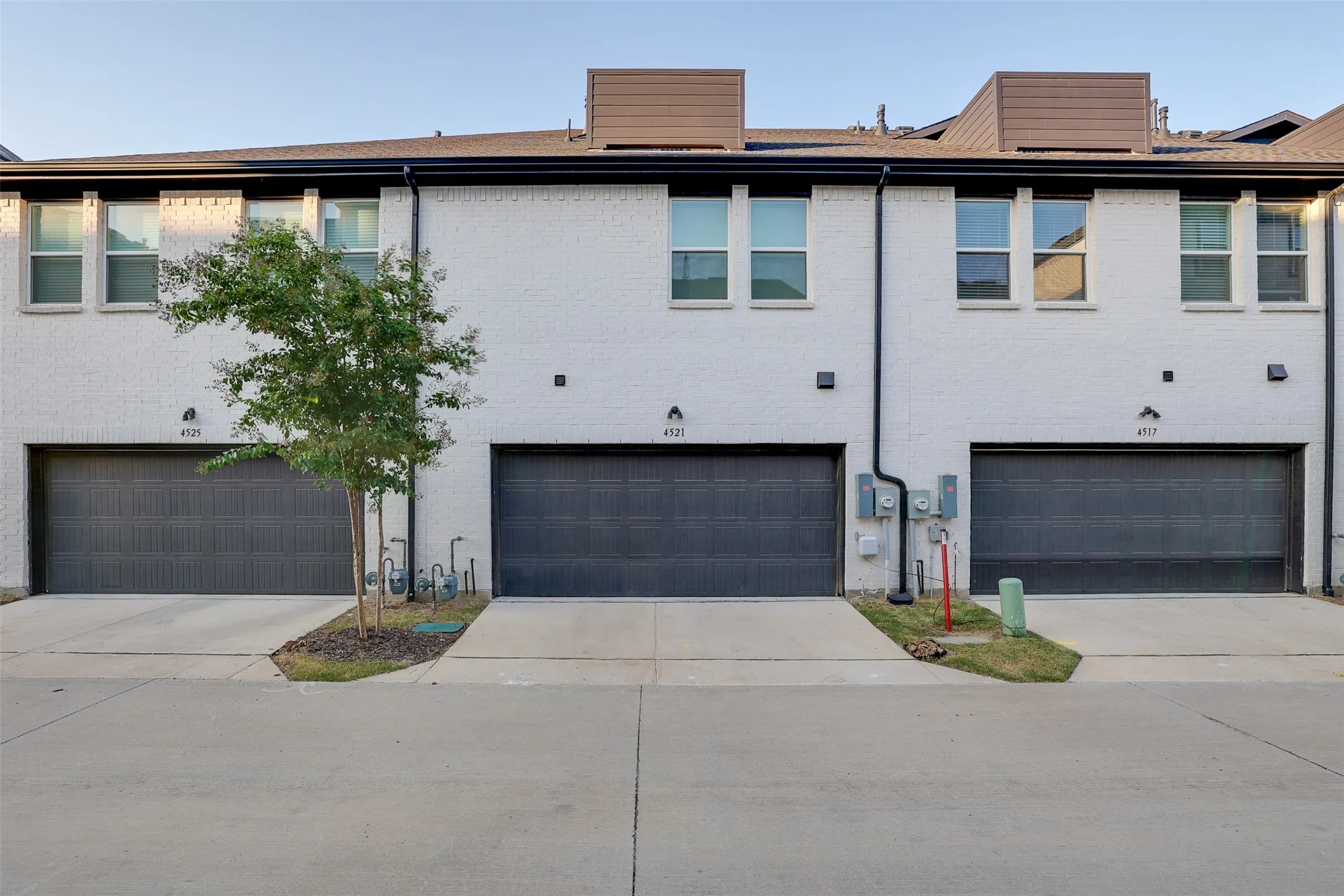 White painted brick exterior with dark gray garage doors, individual driveways, and upper-level windows