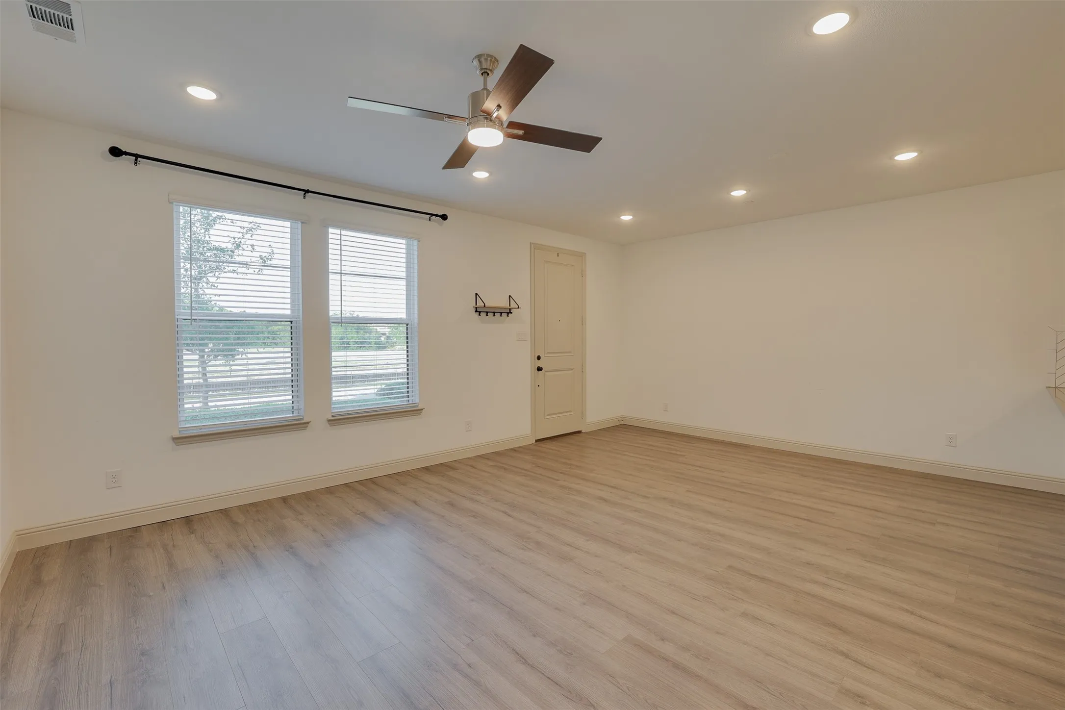 Spacious room featuring wood-finish flooring, recessed lighting, a ceiling fan, and multiple windows with blinds