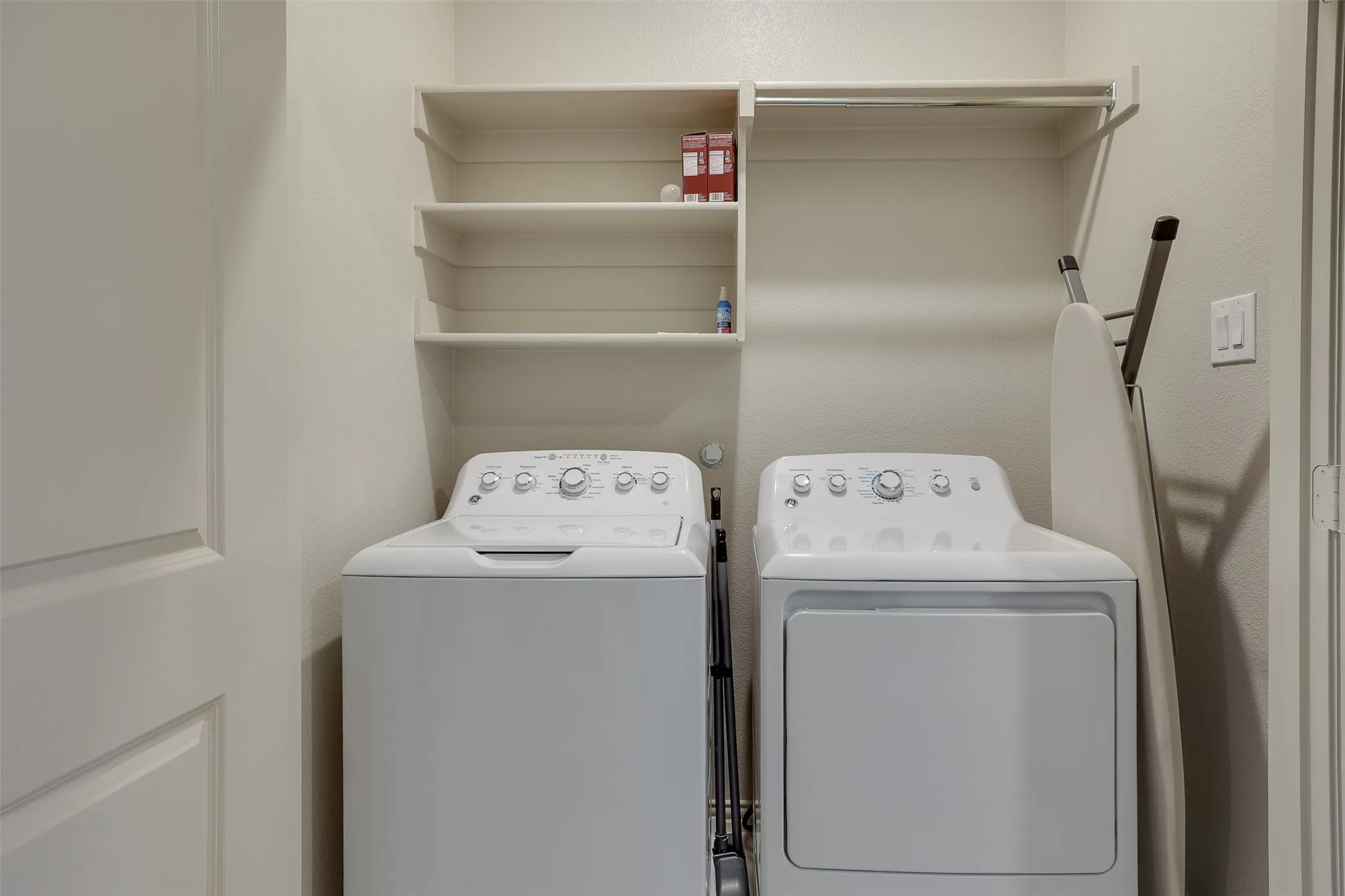 Laundry area featuring a top-load washer, front-load dryer, built-in shelving, and a hanging rod