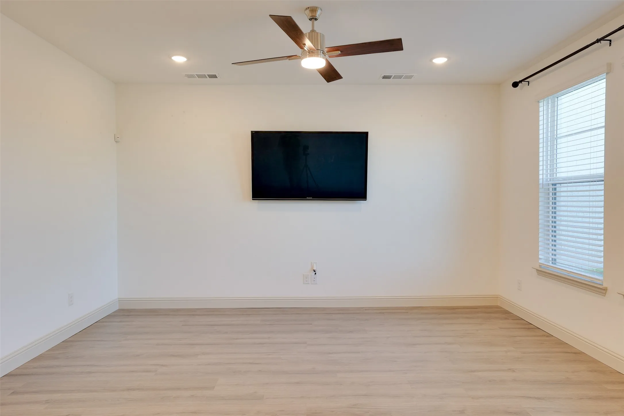 Recessed ceiling lighting, wood-finish flooring, ceiling fan with integrated lighting, wall-mounted display, and window with blinds