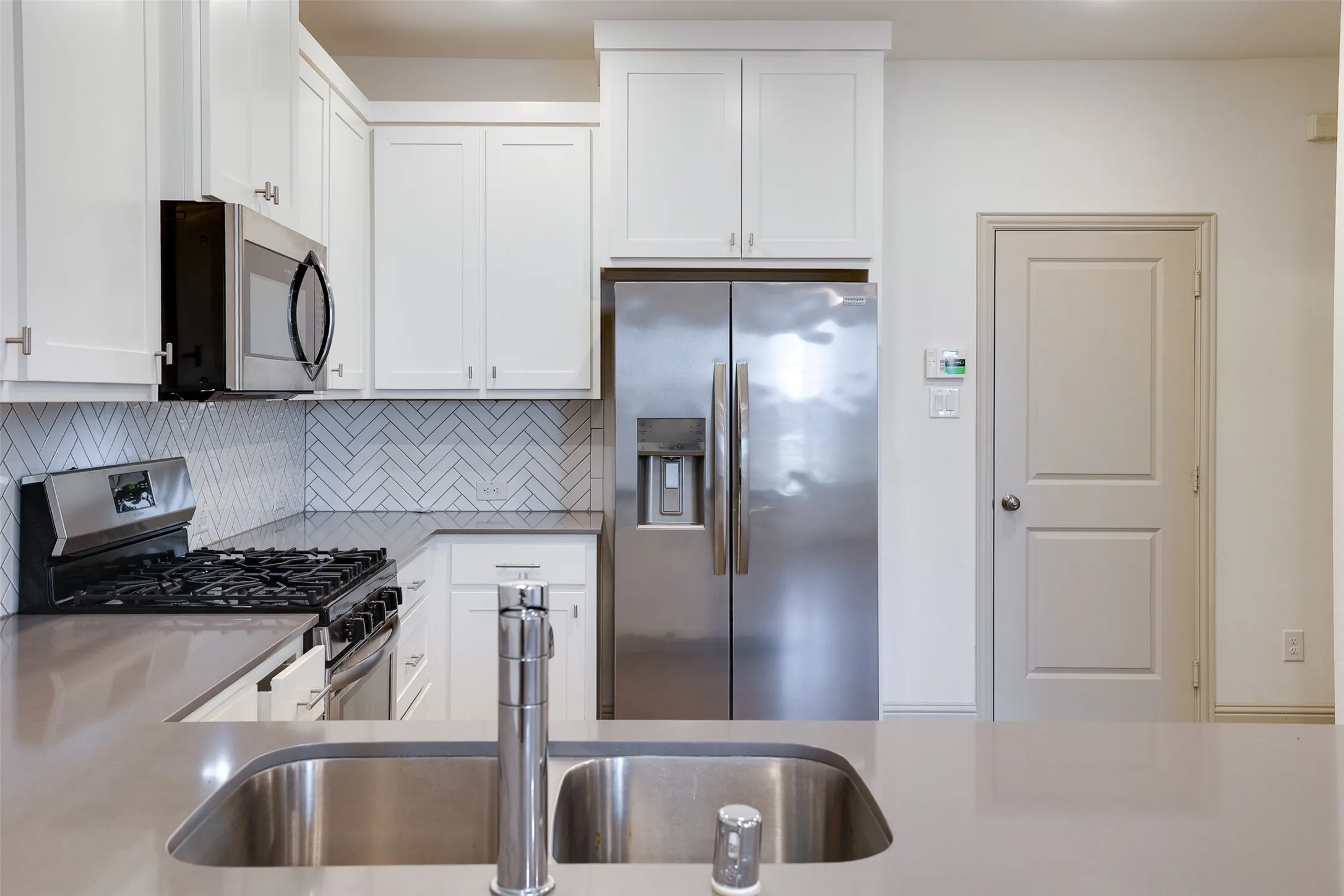 Modern kitchen featuring white shaker cabinetry, stainless steel appliances, a herringbone tile backsplash, and solid surface countertops