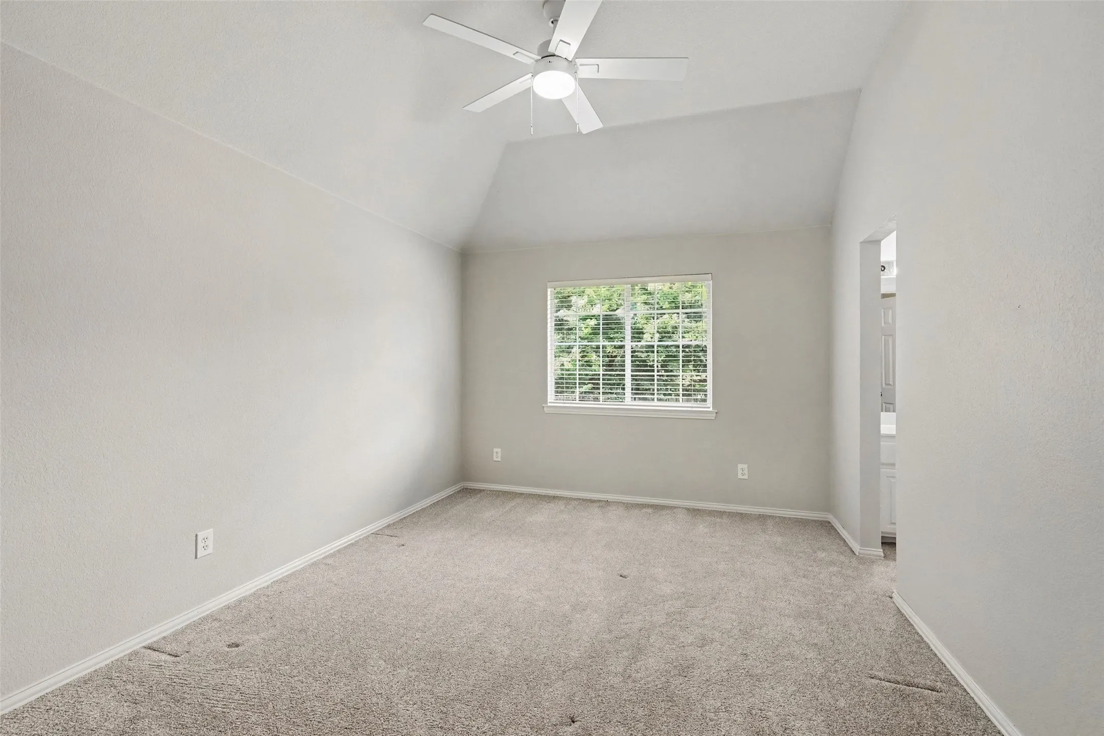 Vaulted ceiling, ceiling fan, carpet flooring, window with white blinds, and an open doorway