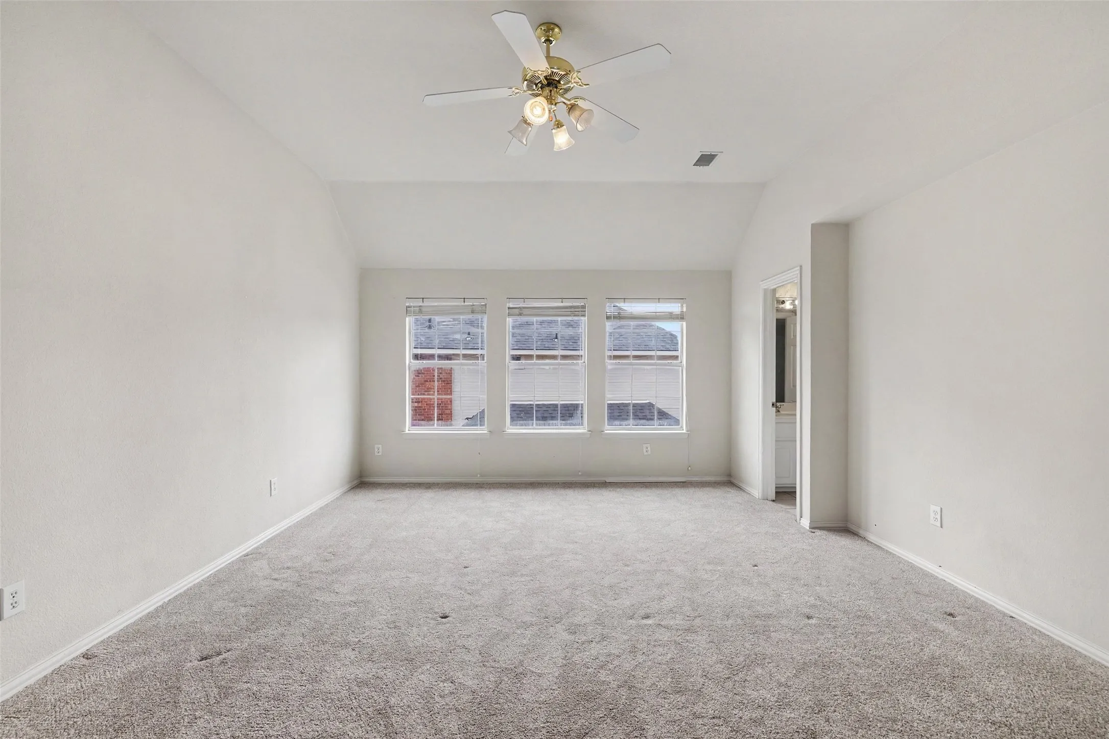 Vaulted ceiling with a ceiling fan, three windows, and plush carpet flooring