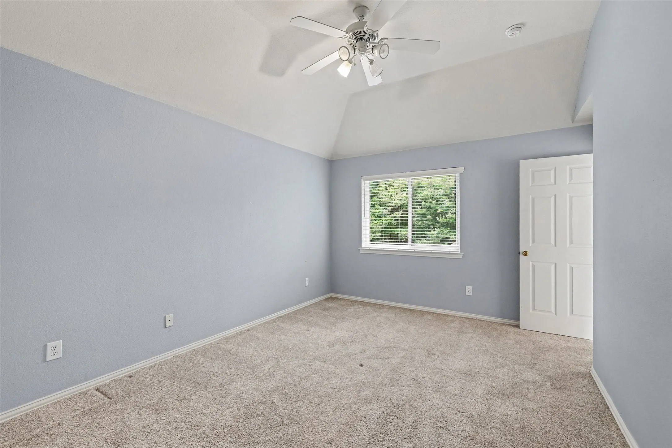 Room featuring vaulted ceilings, plush carpet flooring, a ceiling fan with integrated lighting, a window with blinds, and a paneled door