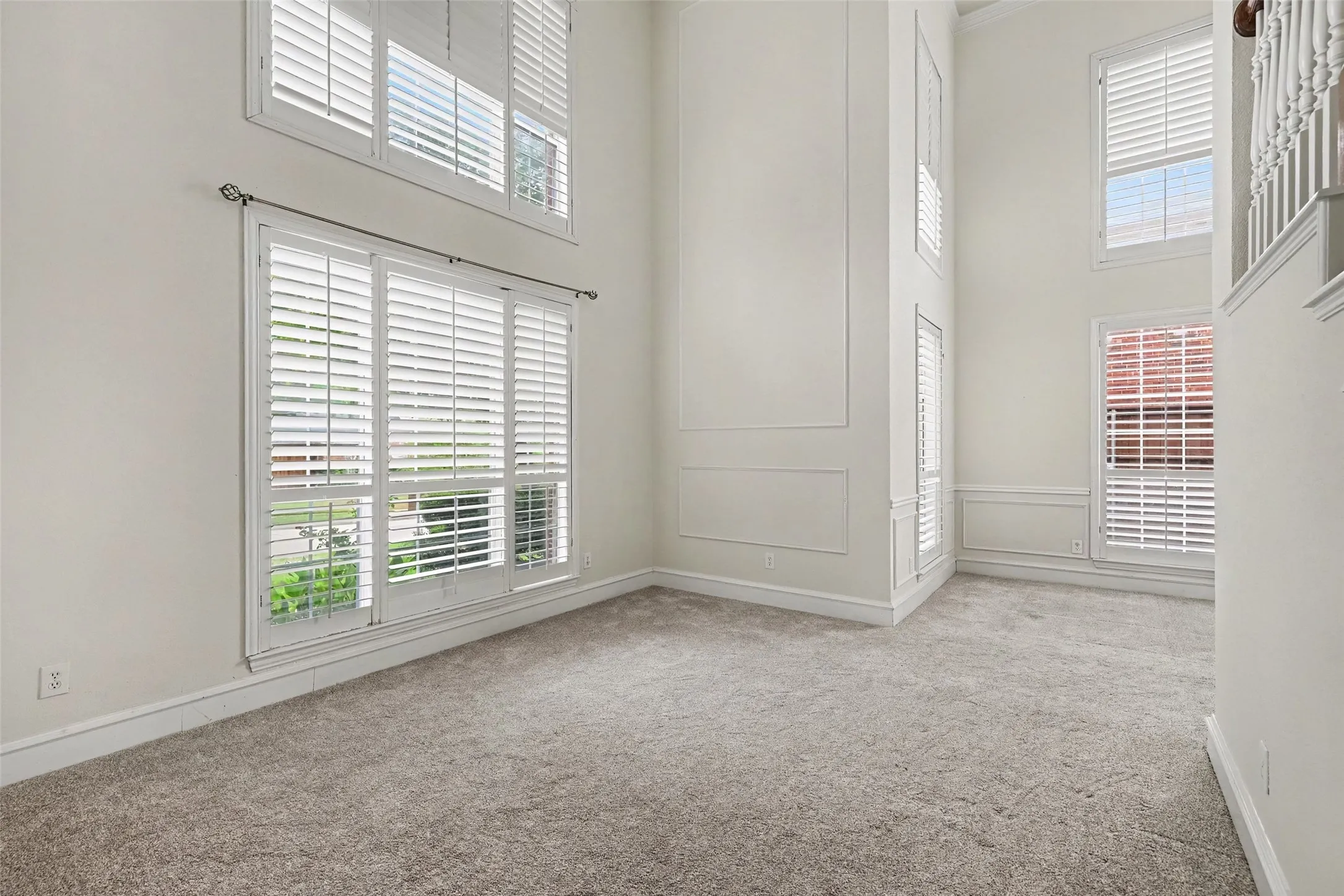 Two-story ceiling, multiple windows with white plantation shutters, decorative wall molding, and plush carpeting