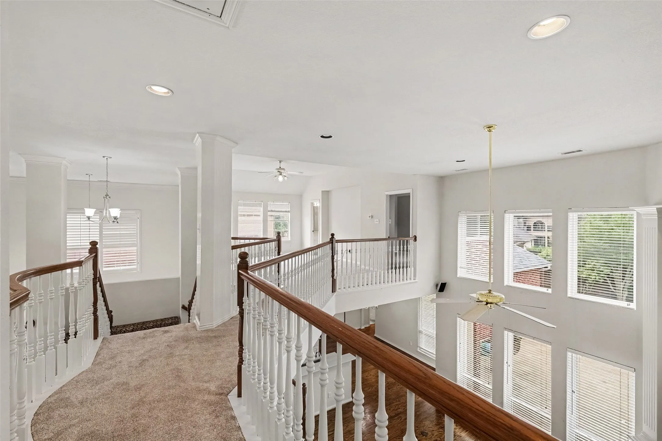 Open concept upper level featuring carpeted flooring, wood-finish handrails, white balusters, recessed lighting, and multiple windows