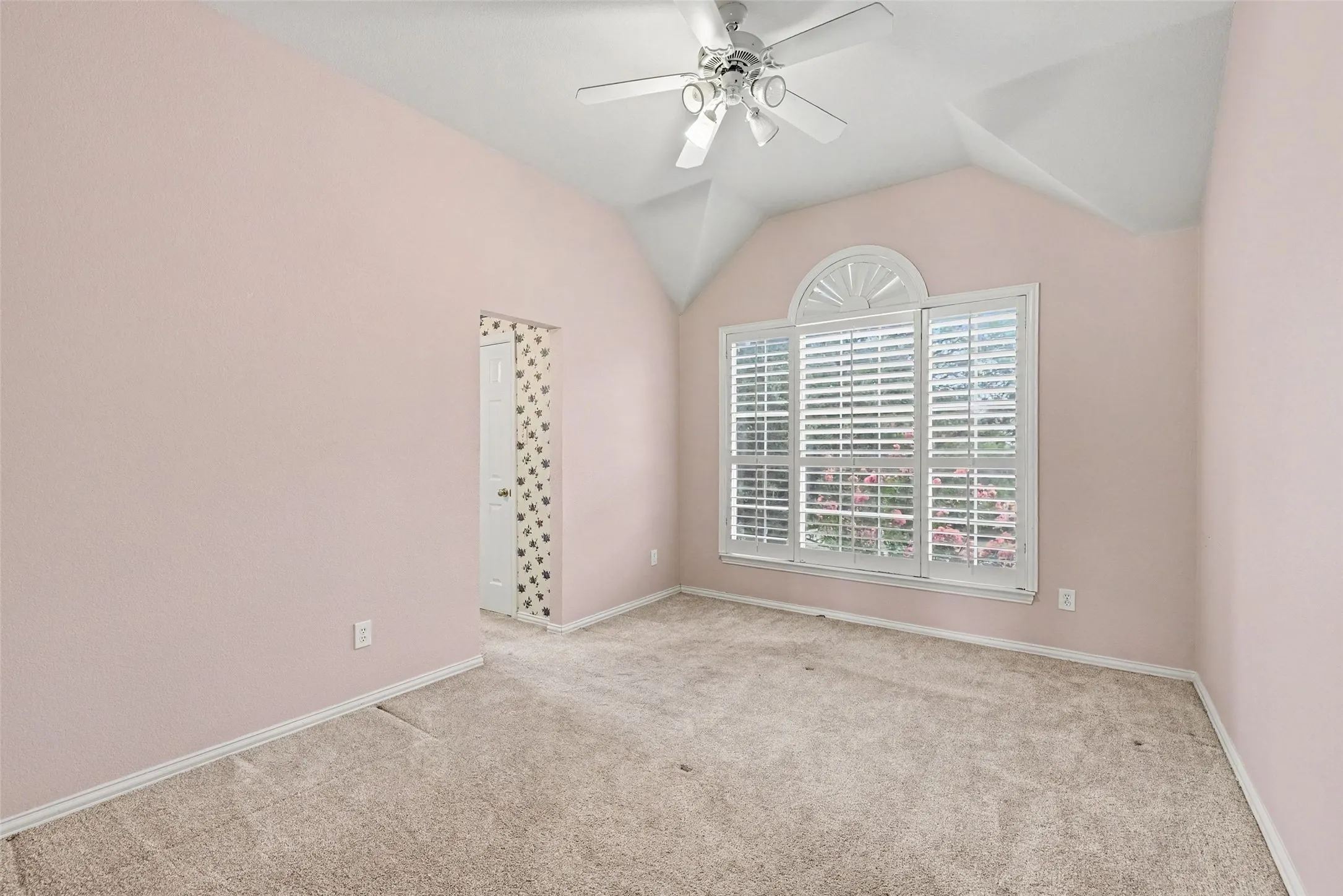 Vaulted ceiling with an attached ceiling fan, arched window with plantation shutters, carpeted flooring, and a white interior door
