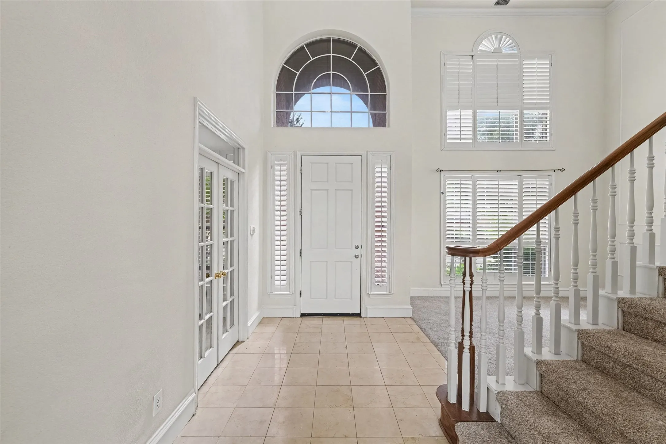 Two-story foyer with high ceilings, arched transom window, ceramic tile flooring, and French doors