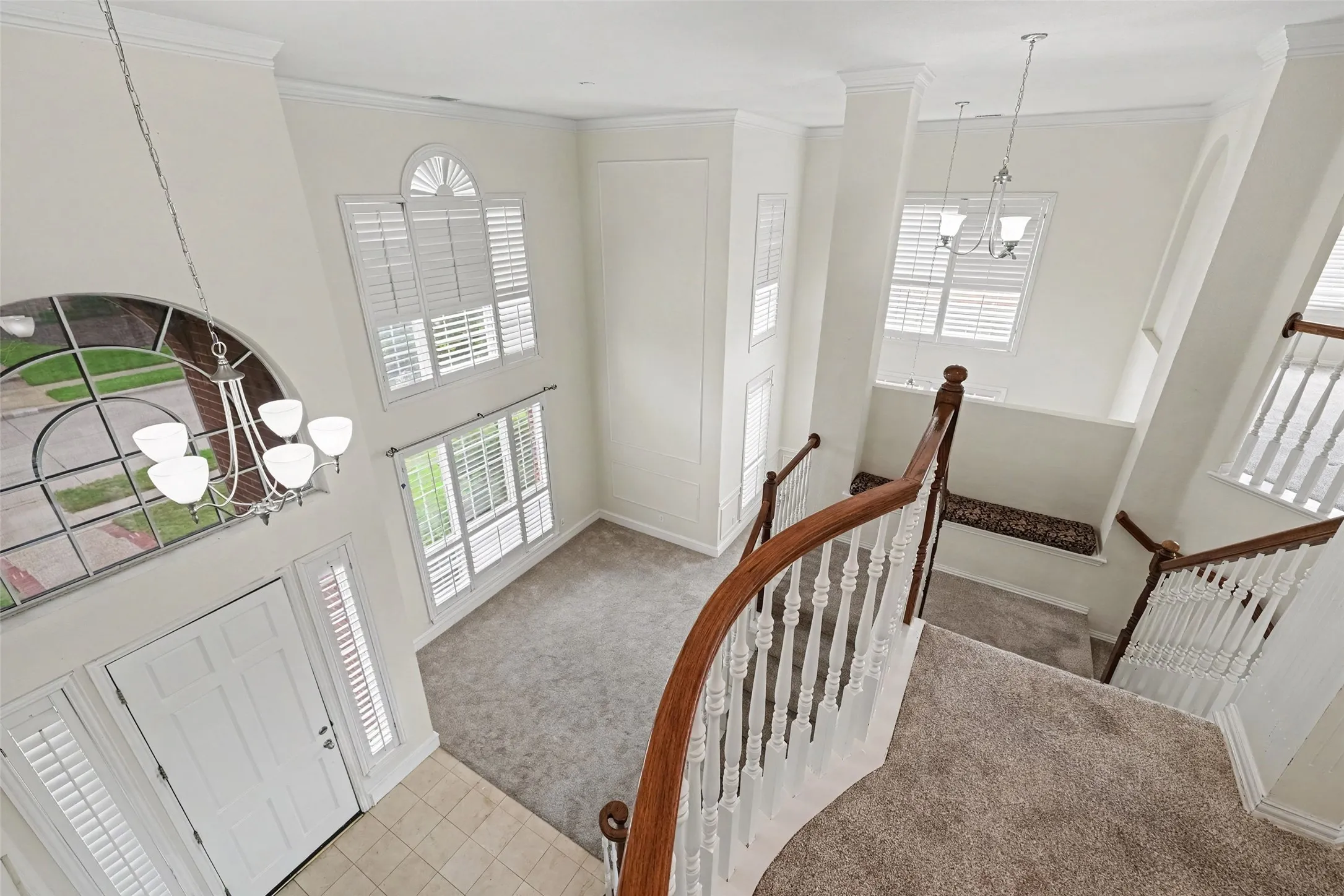 Two-story foyer with a curved wood-finish staircase, large arched window, and overhead chandelier