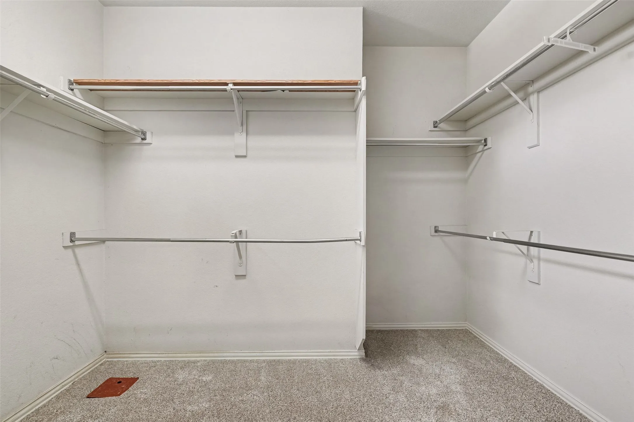 Carpeted walk-in closet with multiple white wire shelves, wood-finish shelving, and metal hanging rods