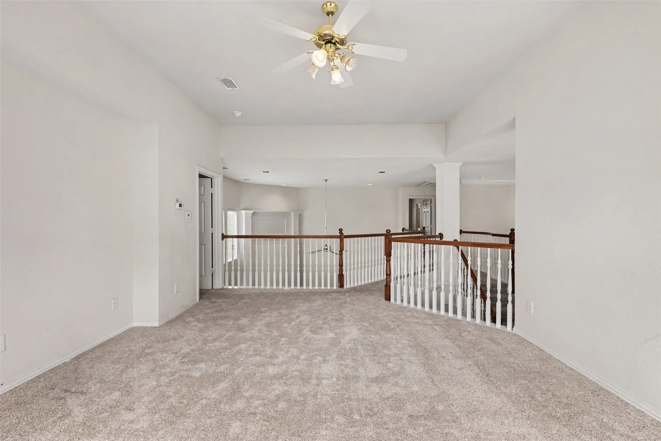 Carpeted open-concept bonus room featuring a ceiling fan, white balustrade railing with wood-finish top rail, and recessed lighting