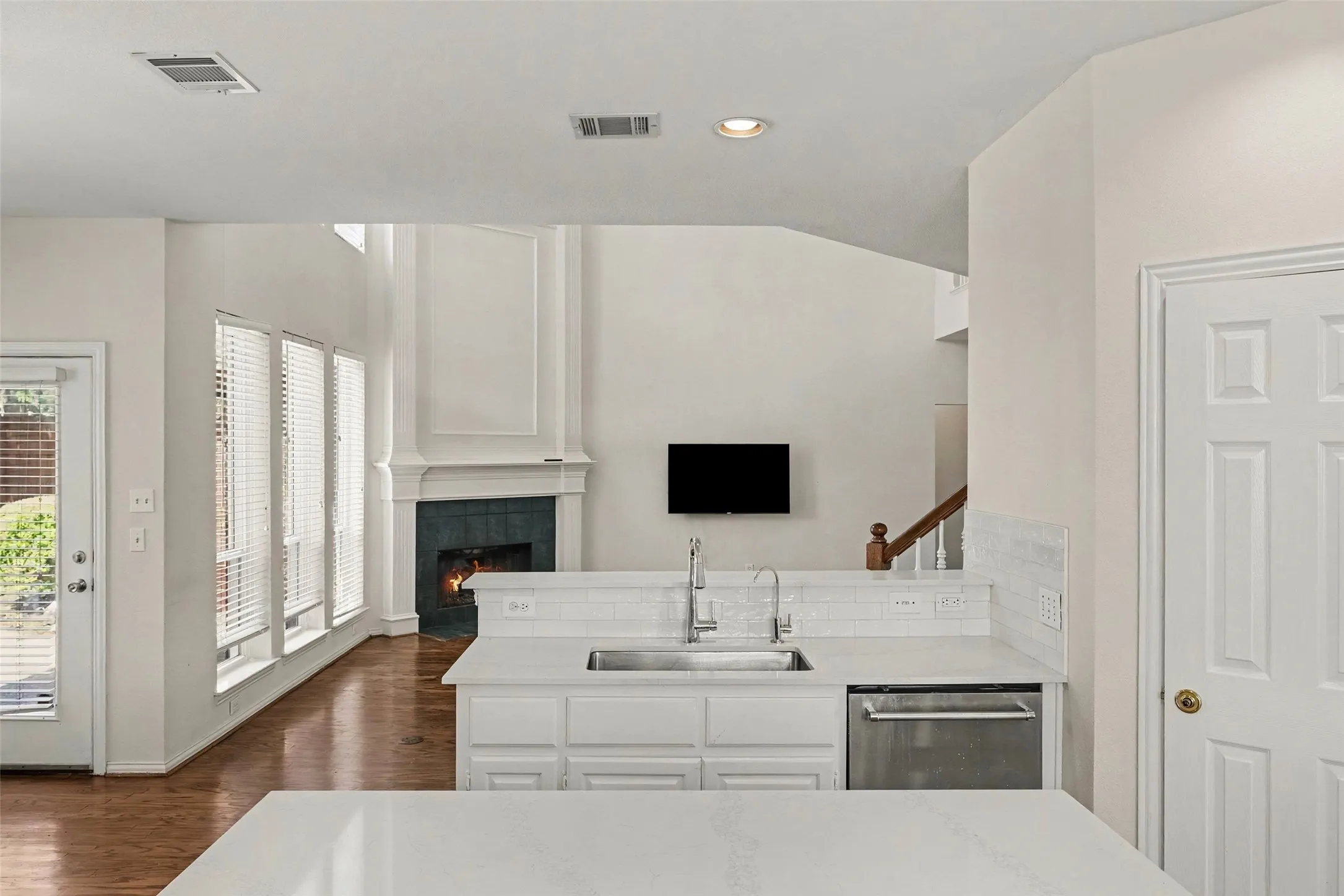 Stainless steel sink, white subway tile backsplash, white cabinetry, integrated dishwasher, and wood-finish flooring