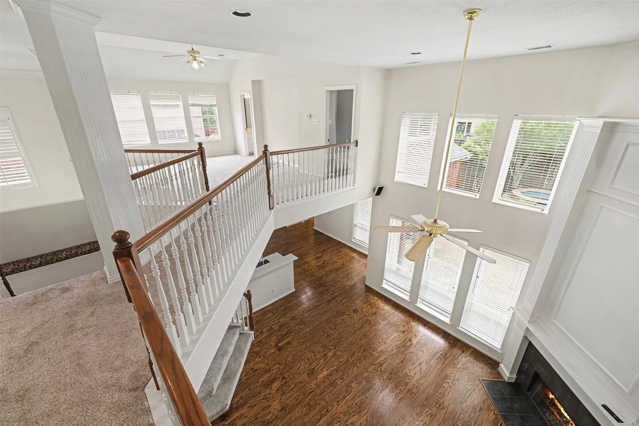 Two-story living area with wood-finish flooring, a fireplace with a dark stone hearth, and multiple windows