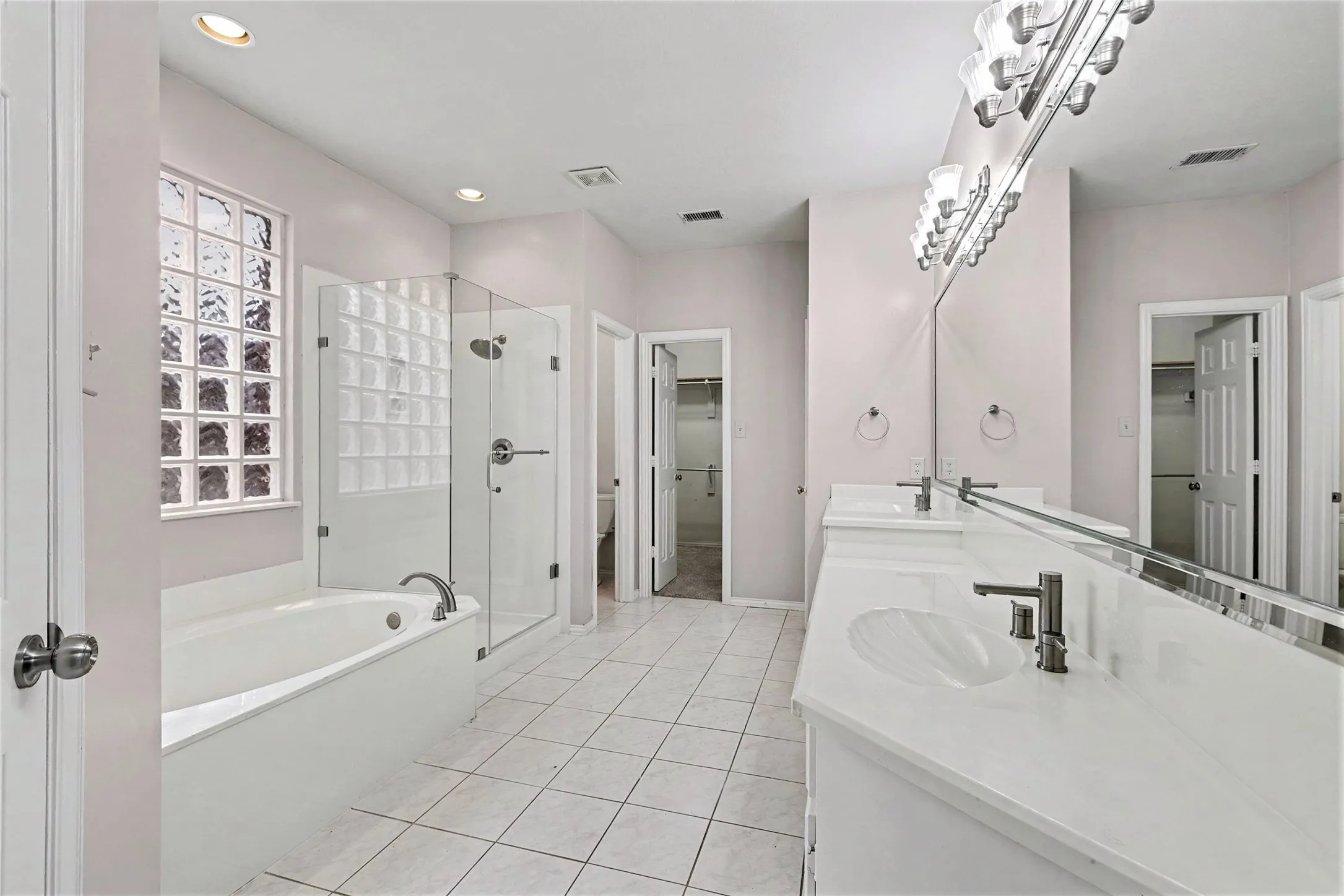 Spa-inspired primary bathroom featuring dual vanities with white quartz countertops, polished chrome fixtures, and an illuminated mirror