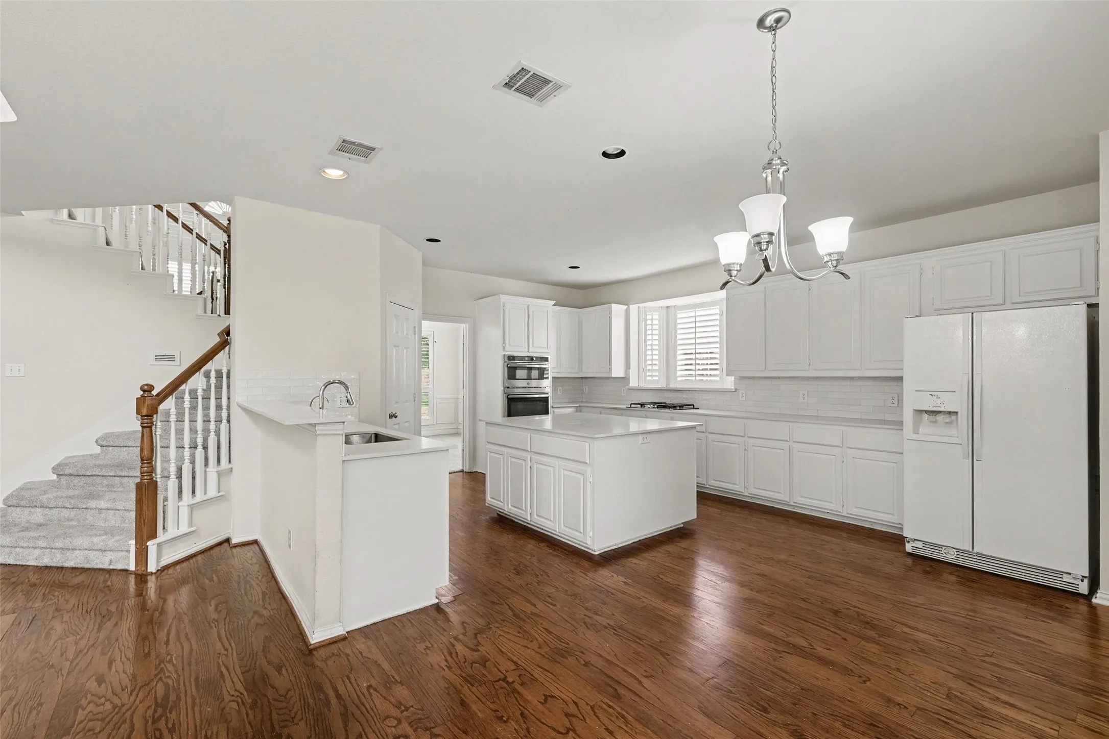 Hardwood flooring, white cabinetry, kitchen island, built-in appliances, and staircase with wood handrail