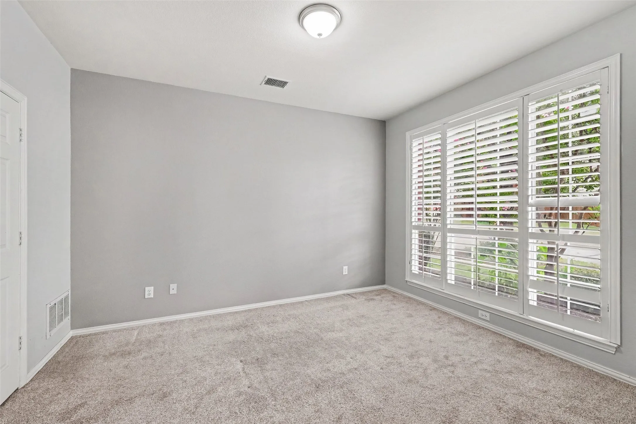 Neutral wall color, carpet flooring, window with white plantation shutters, white trim, and a ceiling-mounted light fixture