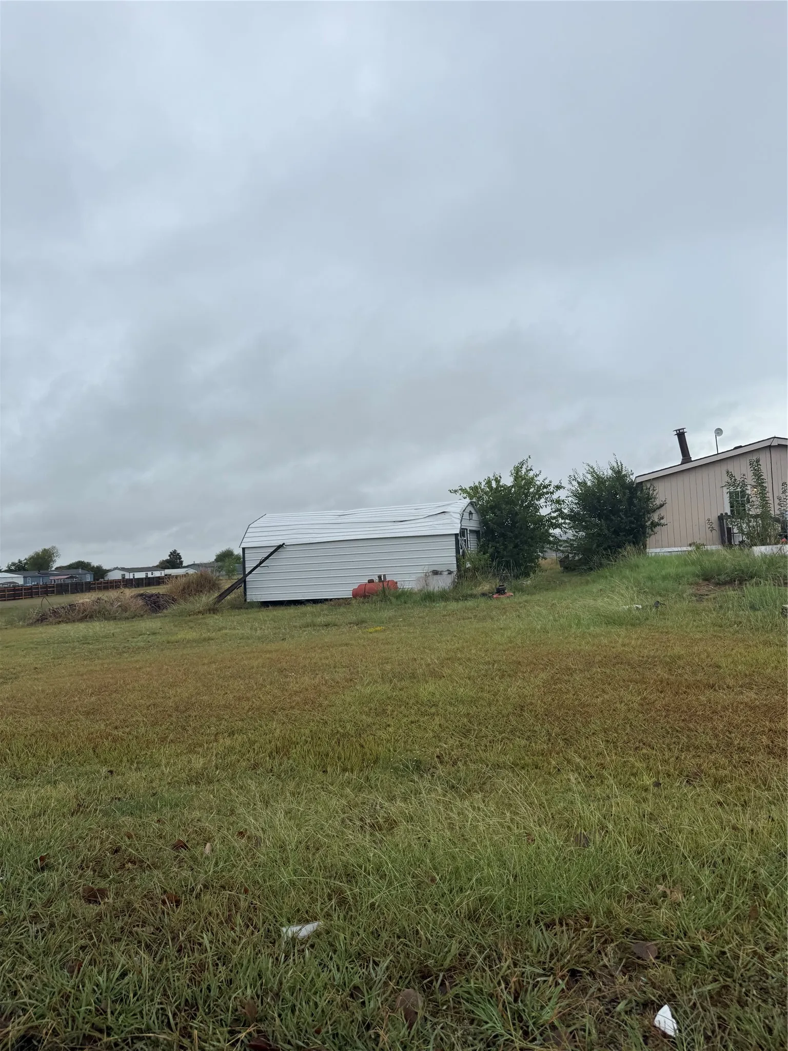 Expansive grass area with a metal storage building featuring a curved roof and a separate structure with a visible chimney