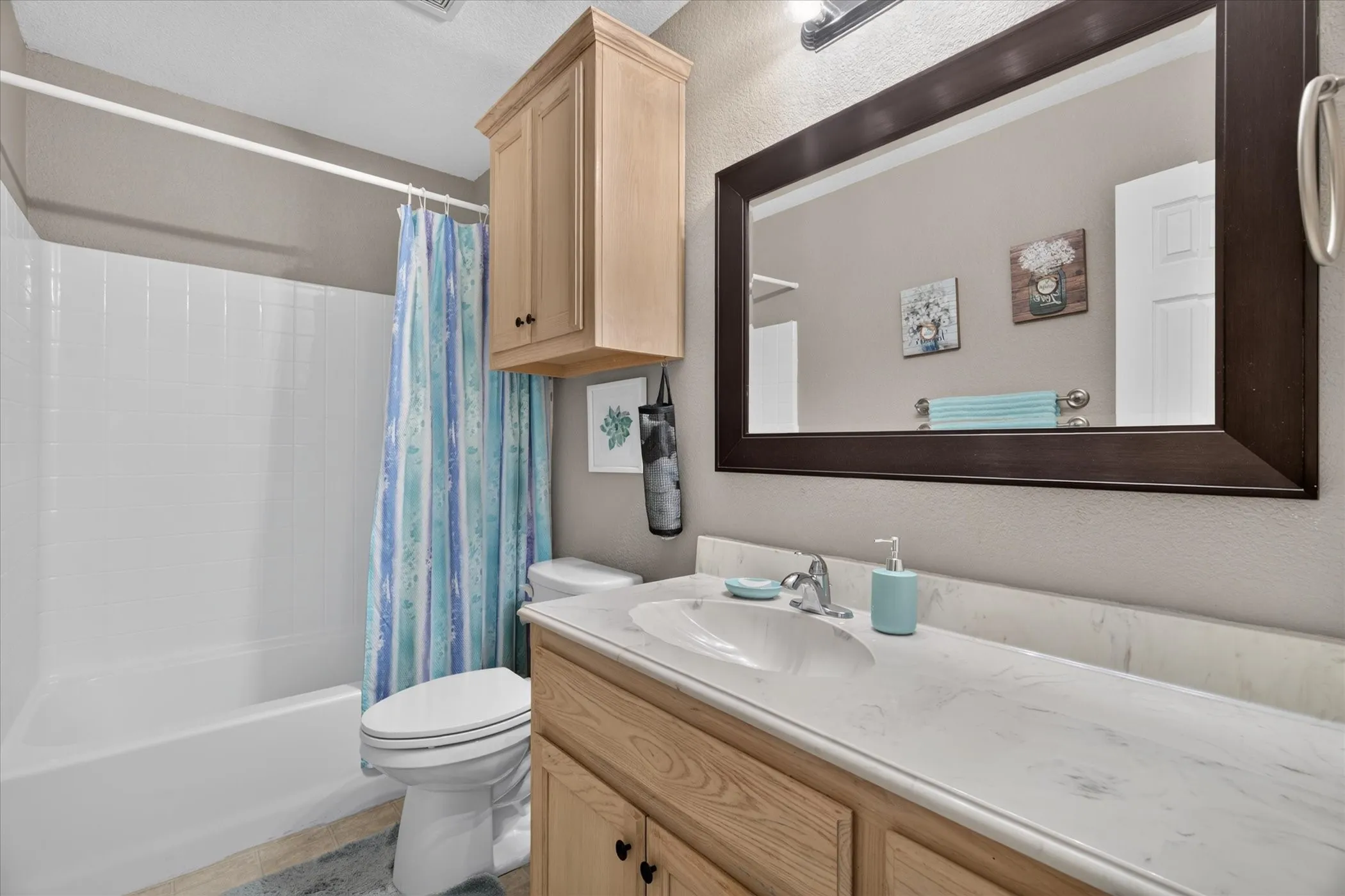 Bathroom featuring a light-tone wood vanity with a stone-finish countertop, integrated sink, wall-mounted storage cabinet, and framed mirror
