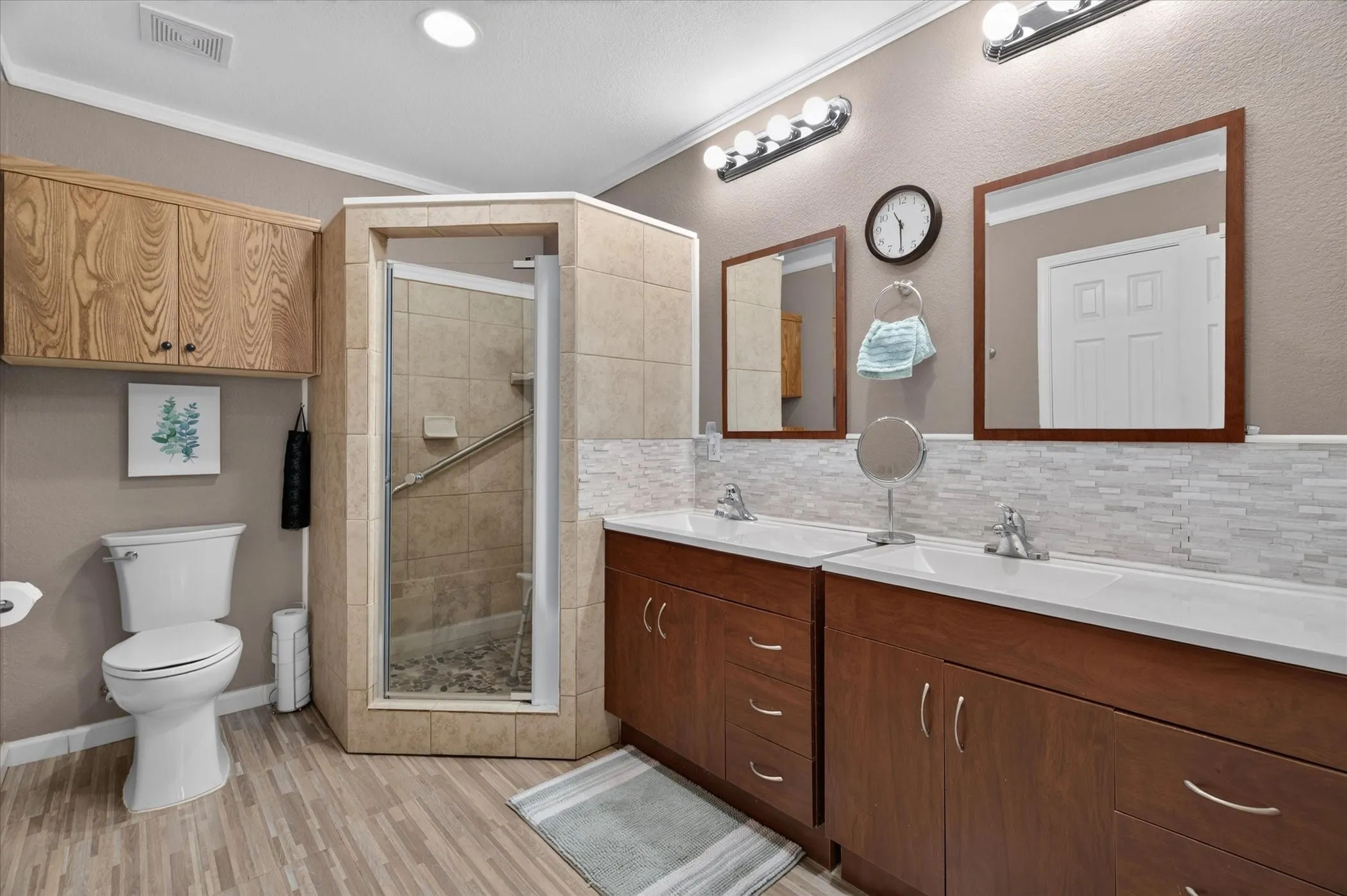 Dual-sink vanity with dark wood-finish cabinetry, rectangular integrated sinks, mosaic tile backsplash, corner shower with tile surround, and built-in upper cabinetry