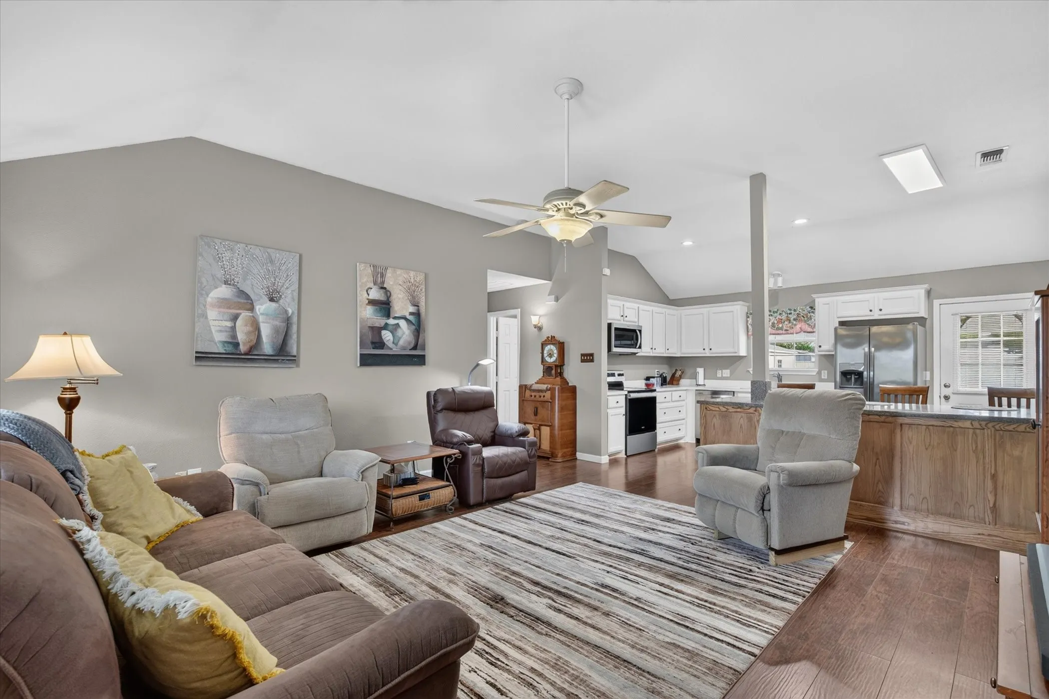 Vaulted ceilings with a central paddle fan, wood-finish flooring, kitchen cabinetry with built-in microwave, and a stone-topped breakfast bar