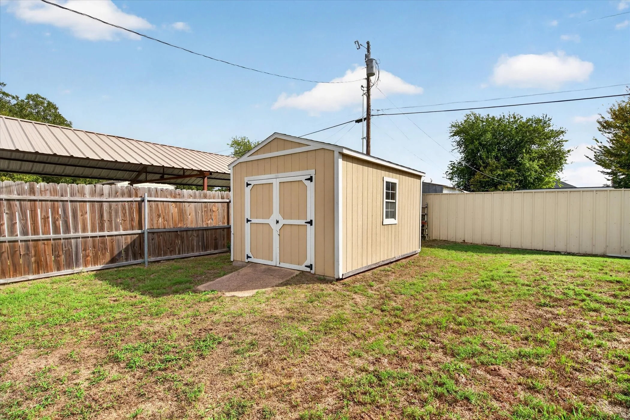 Backyard storage building featuring double entry doors, a single window, and a paved entry pad, enclosed by wood and composite fencing