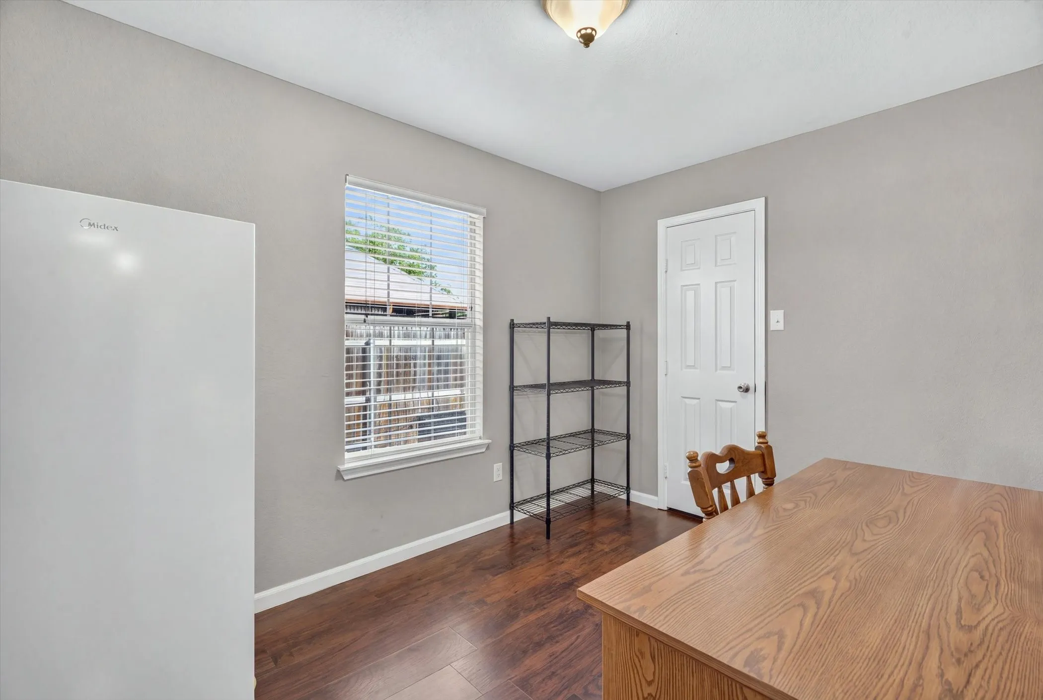 Wood-finish flooring, neutral wall tones, six-panel interior door, and window with horizontal blinds