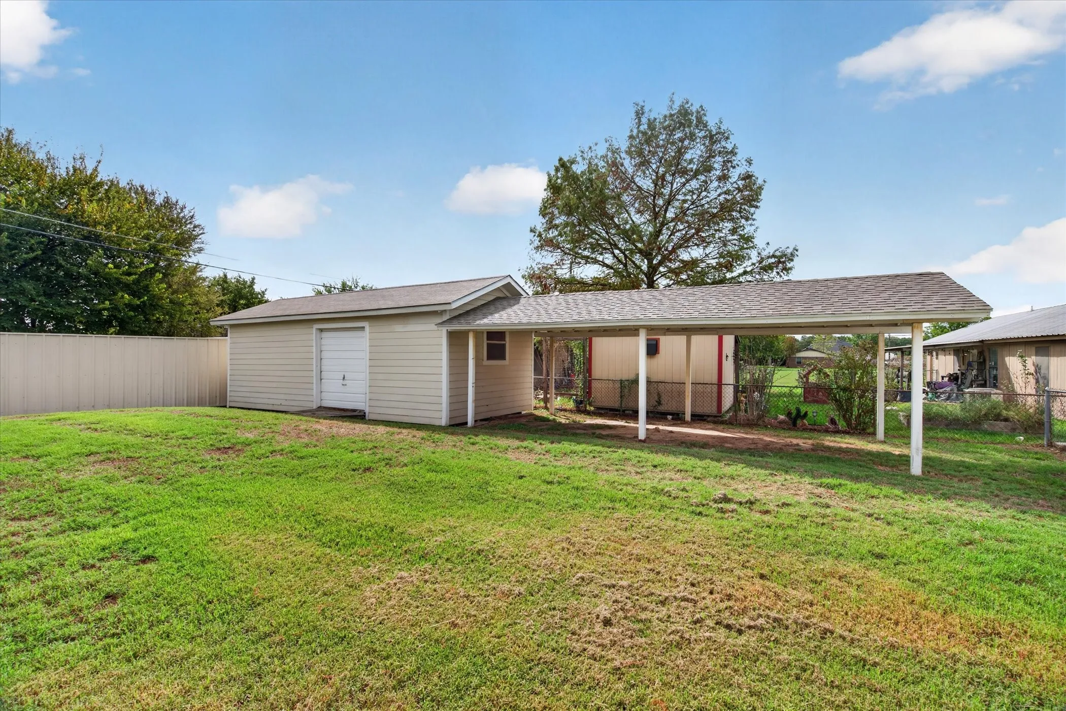 Detached structure featuring vinyl siding, a single-bay garage, an attached covered carport, and a surrounding fenced yard
