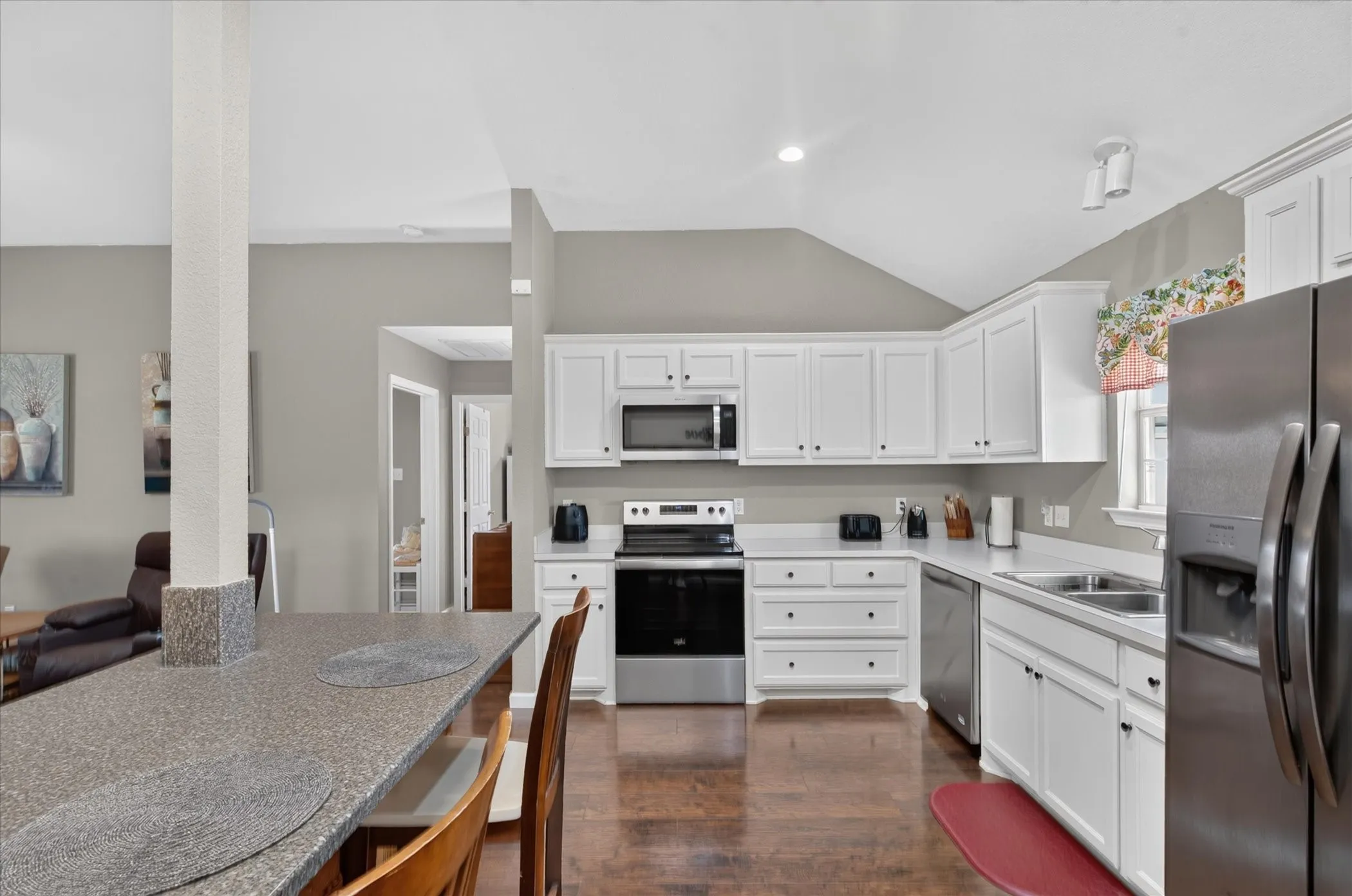 Kitchen featuring white cabinetry, solid-surface countertops, wood-finish flooring, stainless steel appliances, and a vaulted ceiling