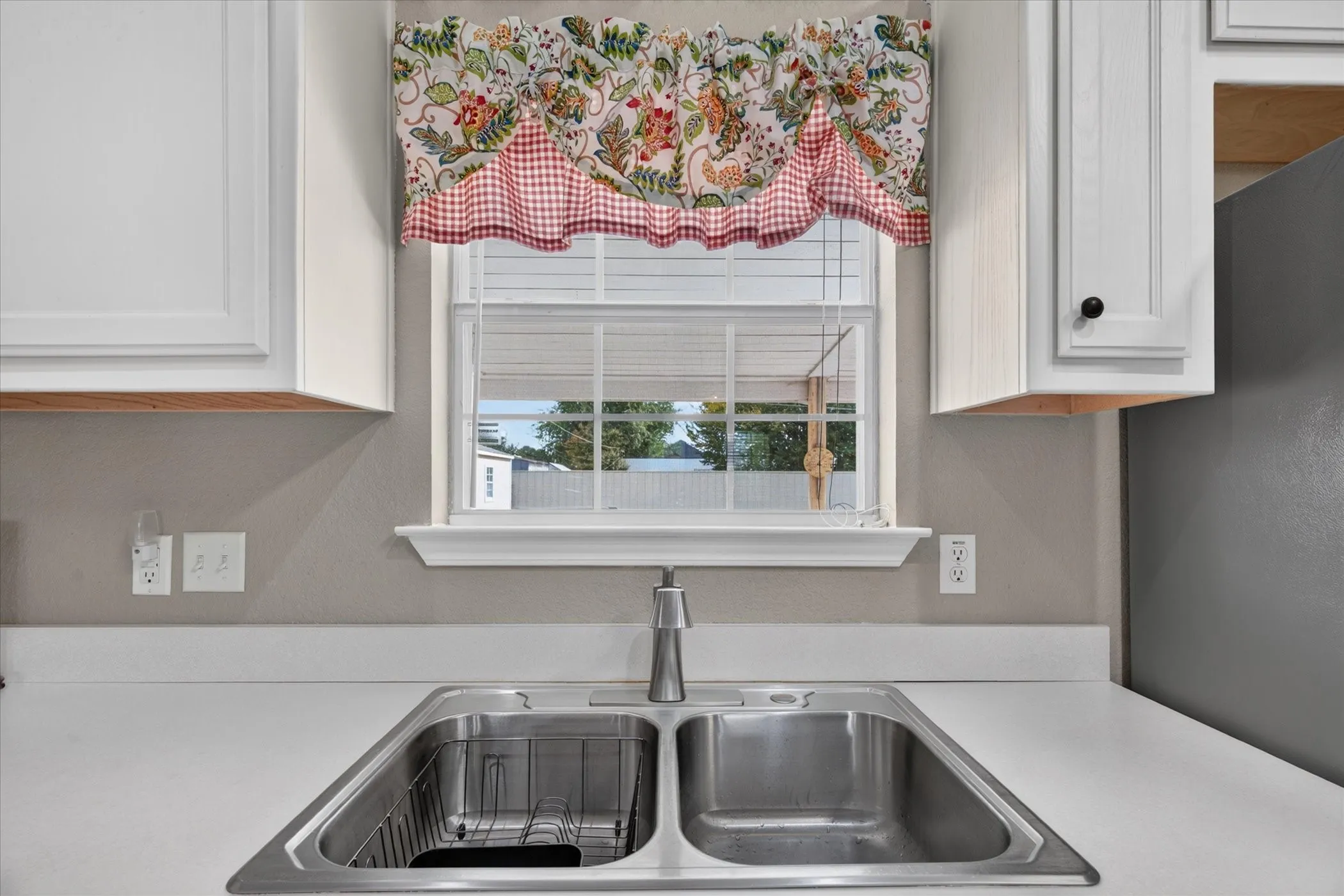 Double-basin stainless steel sink with a high-arch gooseneck faucet, white solid-surface countertops, and shaker-style cabinetry