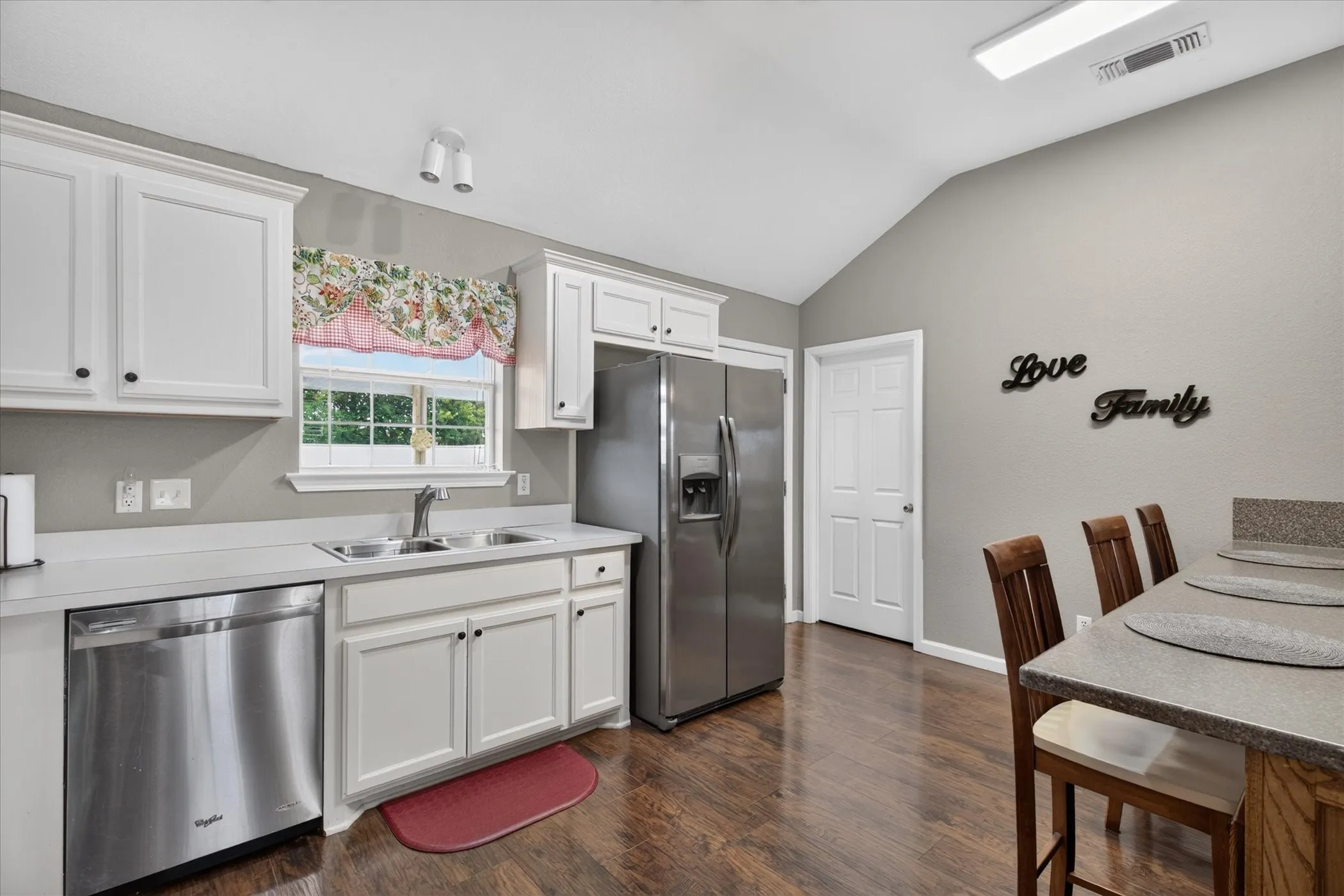 Kitchen featuring vaulted ceilings, wood-finish flooring, white cabinetry, stainless steel appliances, and a built-in peninsula breakfast bar