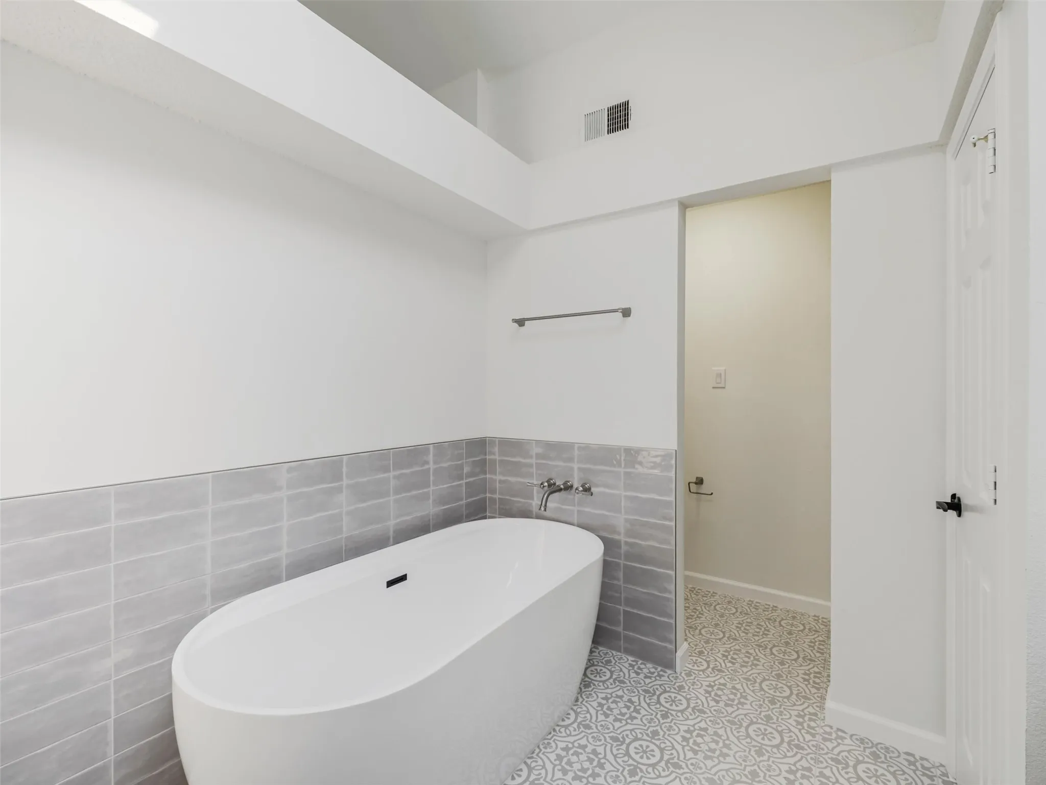 Freestanding soaking tub with wall-mounted faucet, subway tile wainscoting, and patterned floor tile